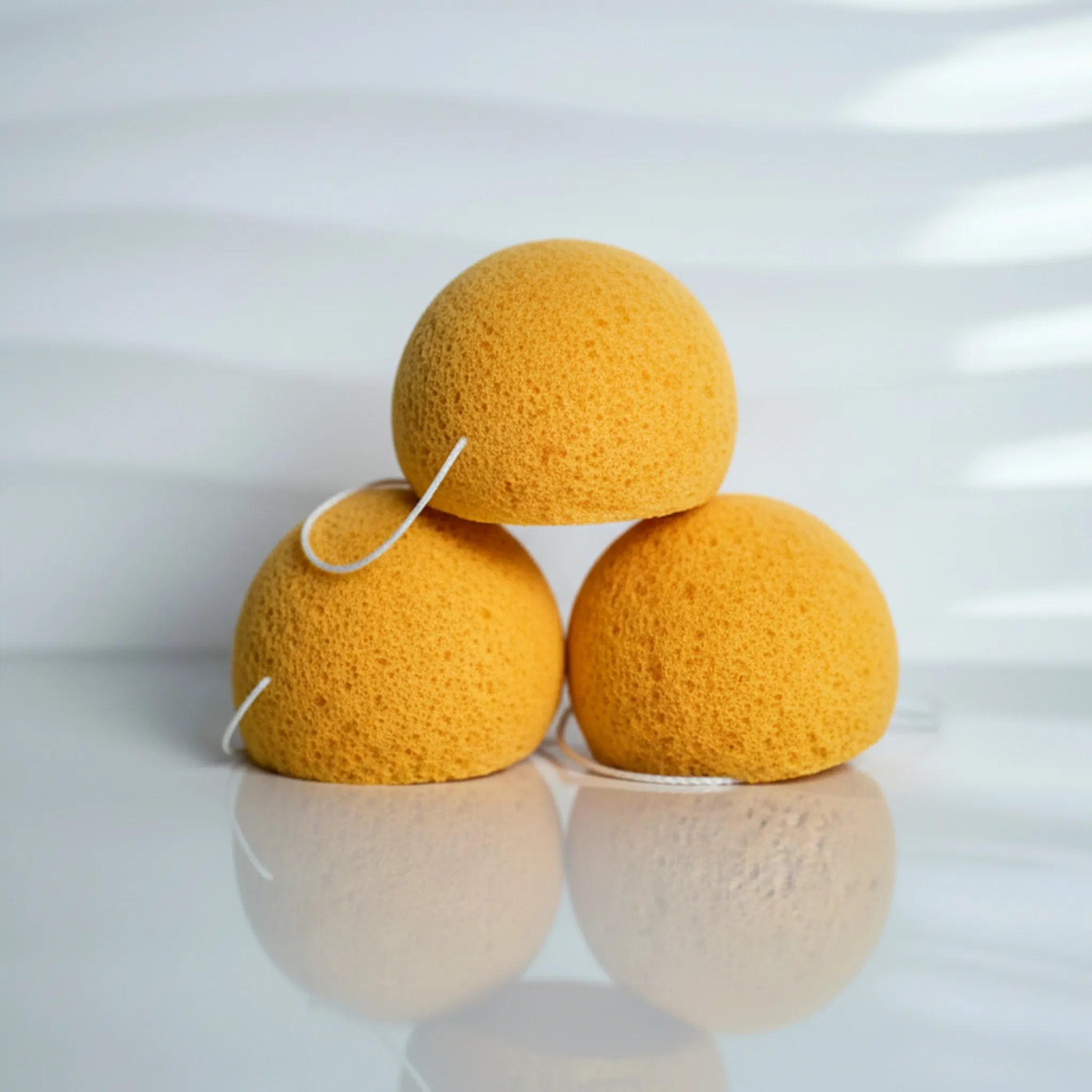 Three turmeric konjac sponges stacked on a reflective surface with a white background