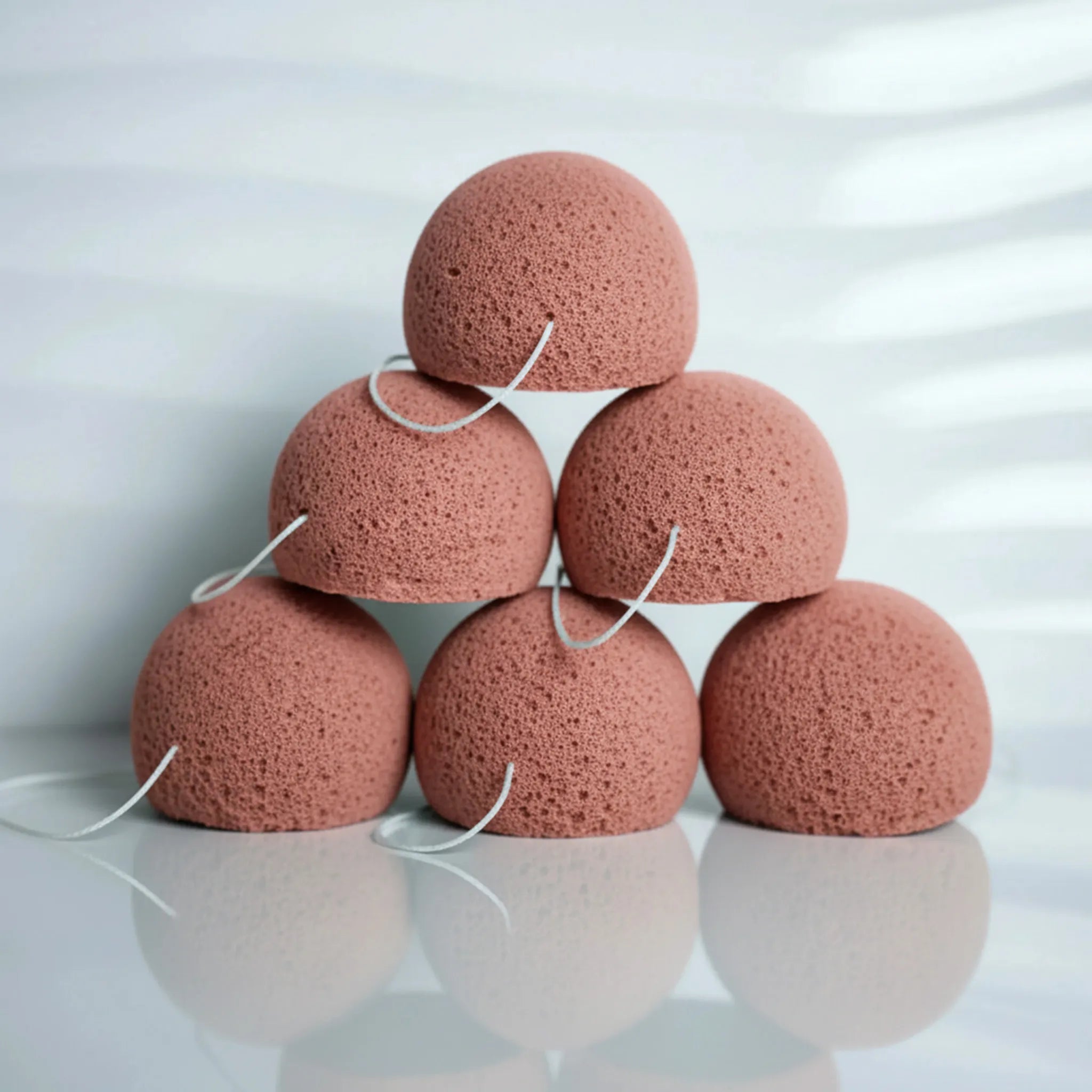 Stack of red clay konjac sponges on a reflective surface with a white background
