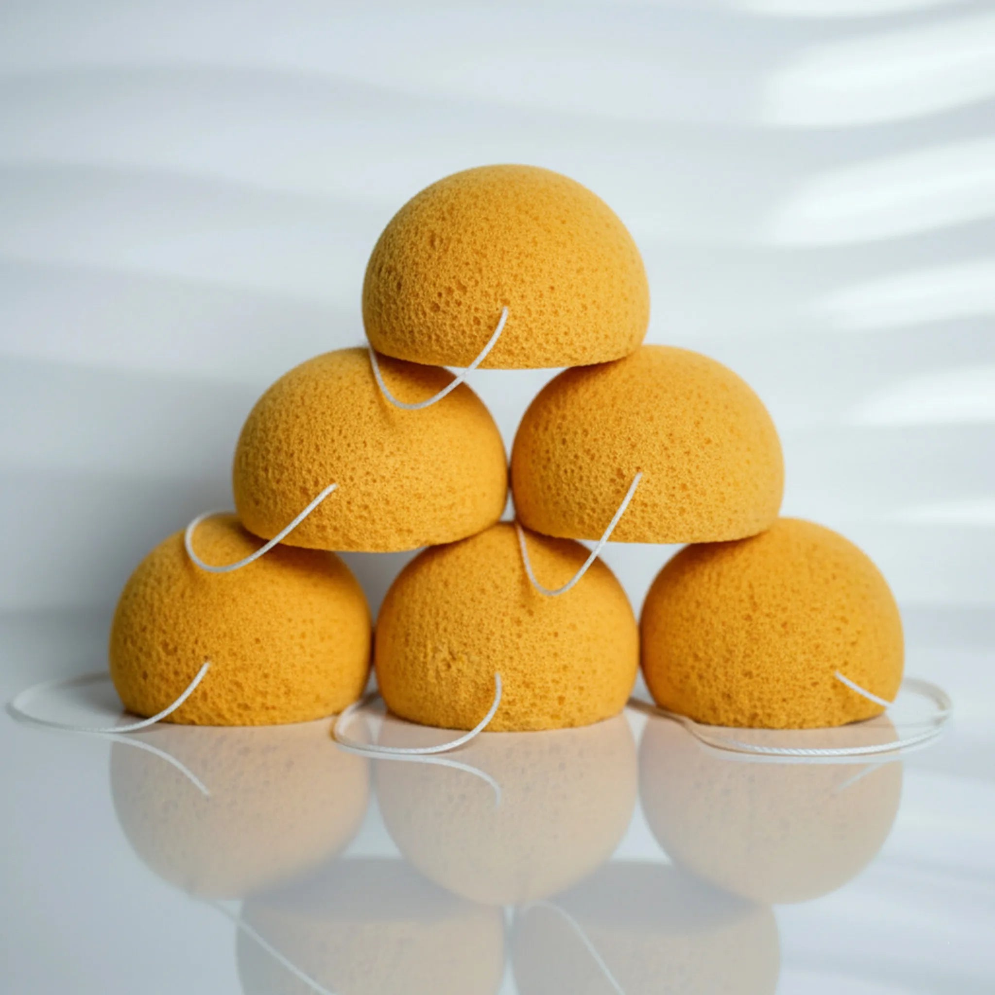 Stack of turmeric konjac sponges on a white surface with a light gray background
