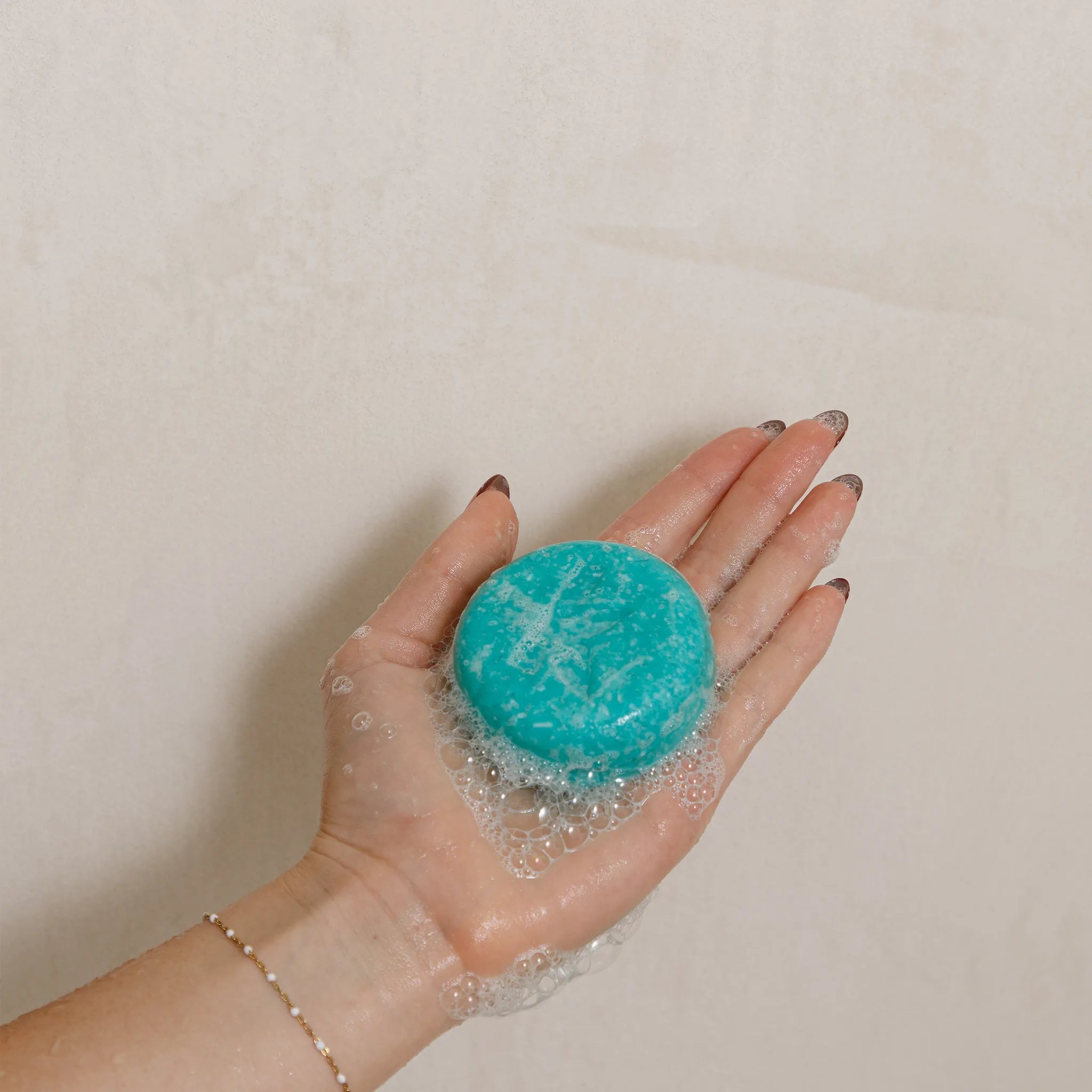 Hand holding a eucalytpus shampoo bar with bubbles against a beige background