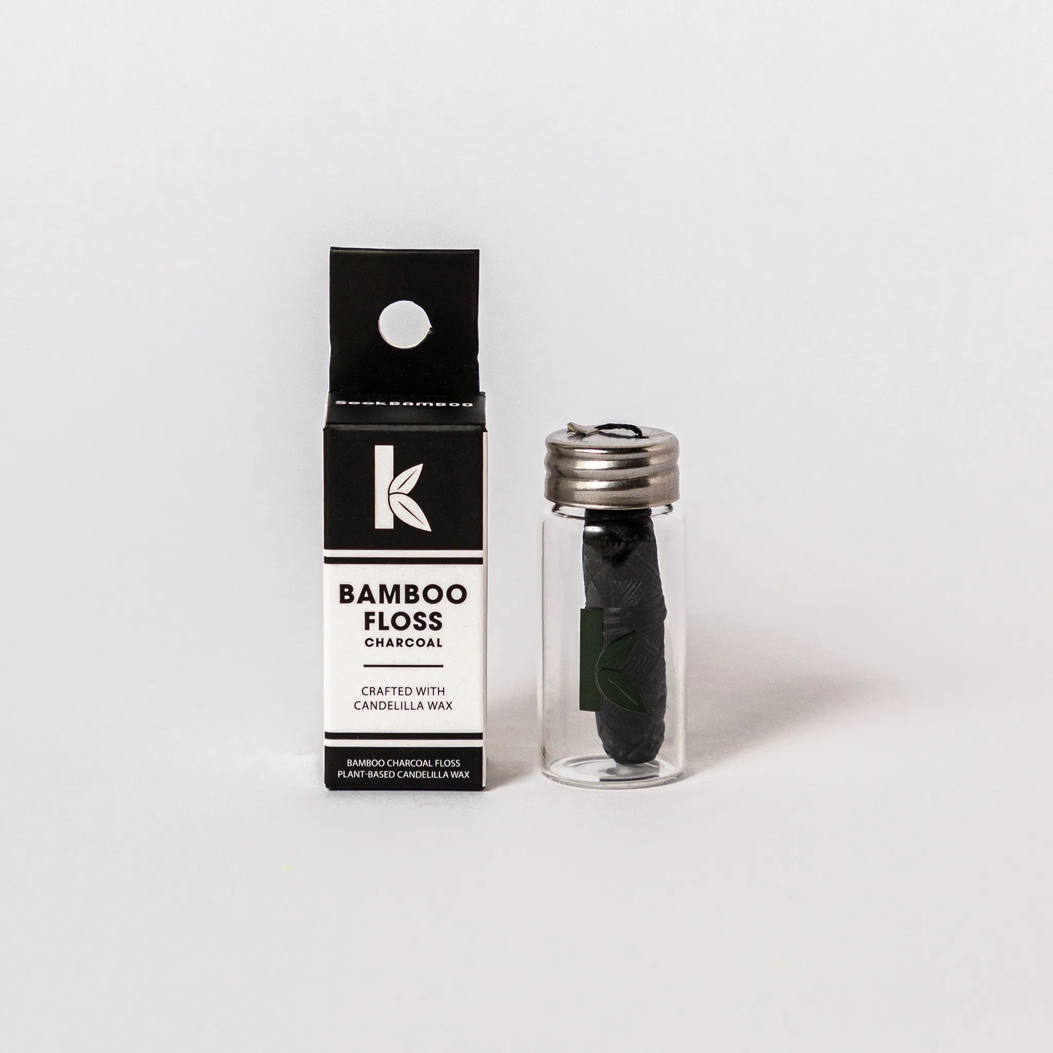 Seek Bamboo Floss Charcoal packaging box next to a clear glass vial containing dark charcoal-colored floss with a silver cap, on a light gray background.
