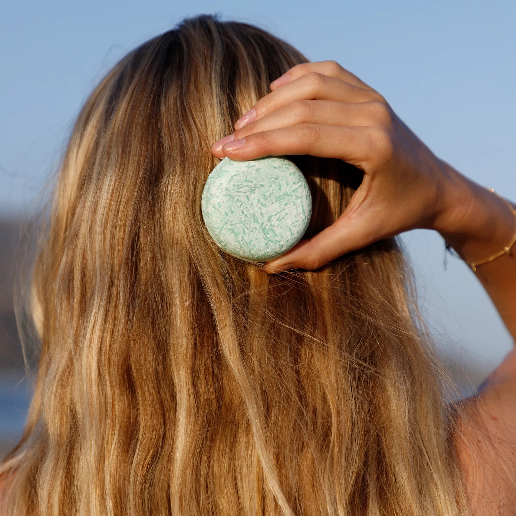 Person holding a biotin shampoo bar against a blurred natural background