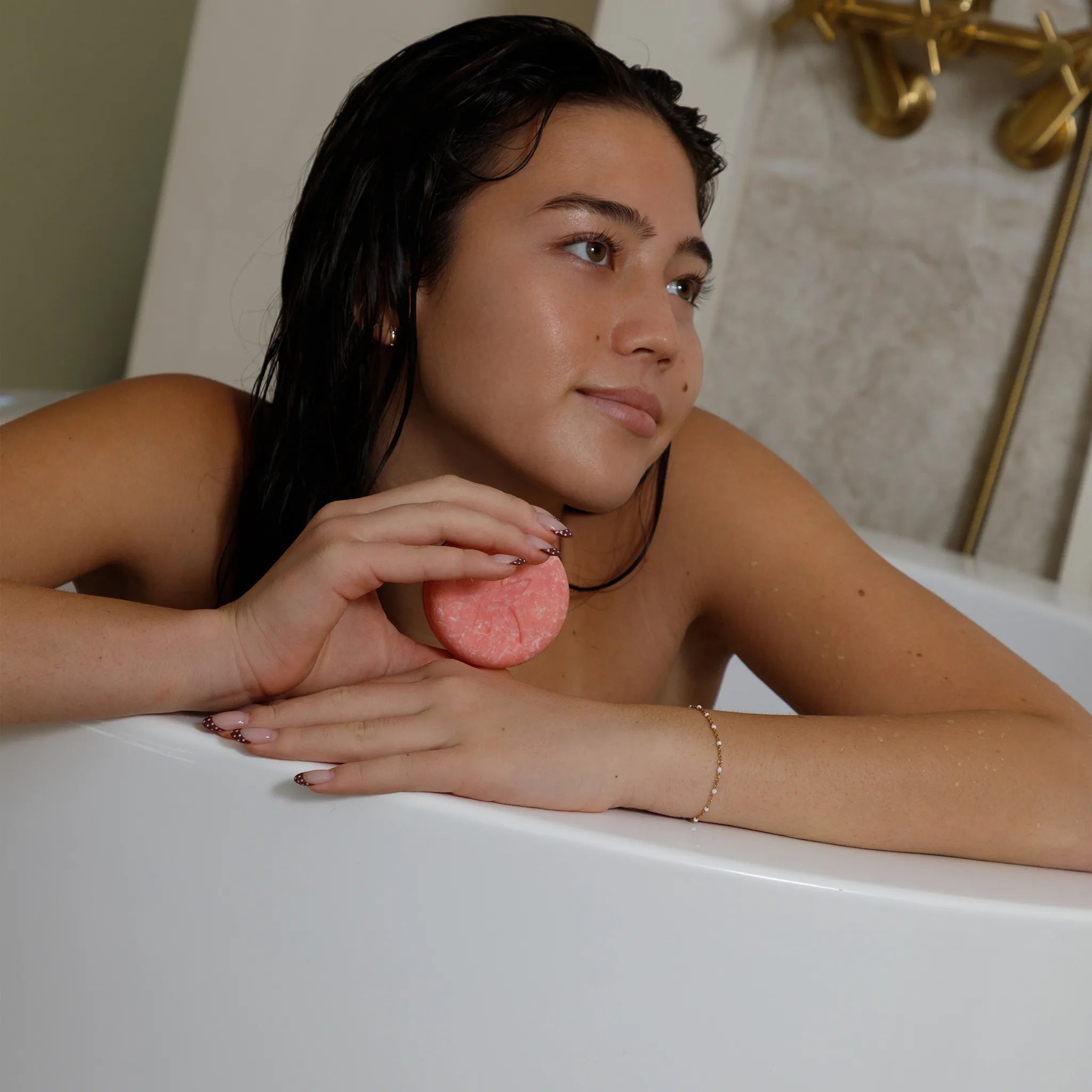 Woman in a bathtub holding a casotr oil shampoo bar