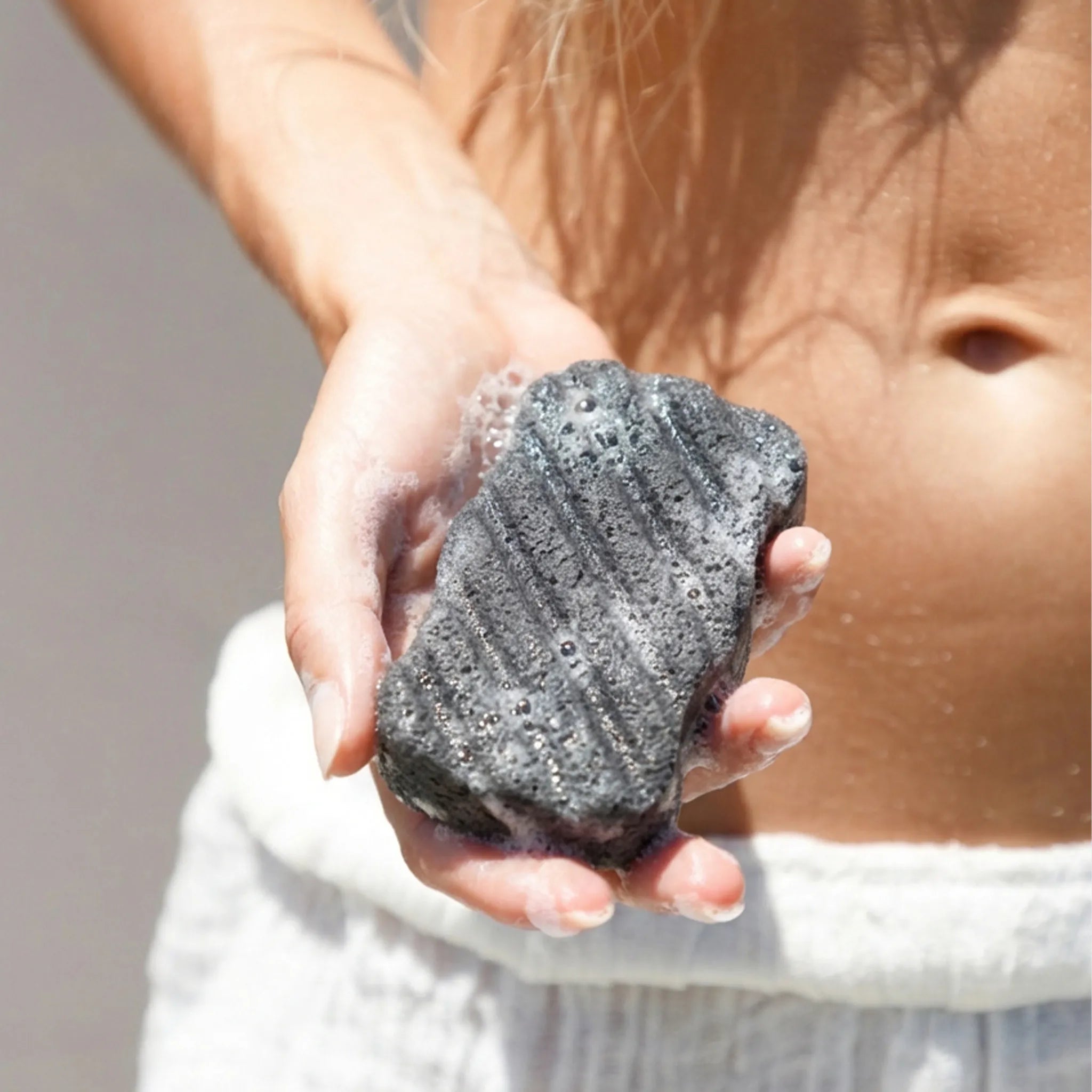 Person holding a gray exfoliating scrubber with soap suds.