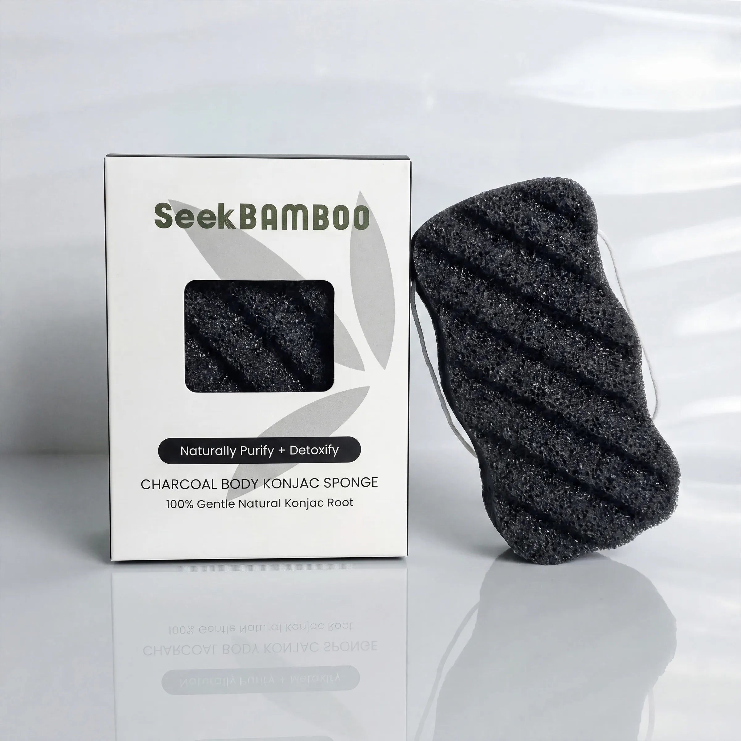 Seek Bamboo charcoal body konjac sponge next to its white packaging box on a reflective white surface.
