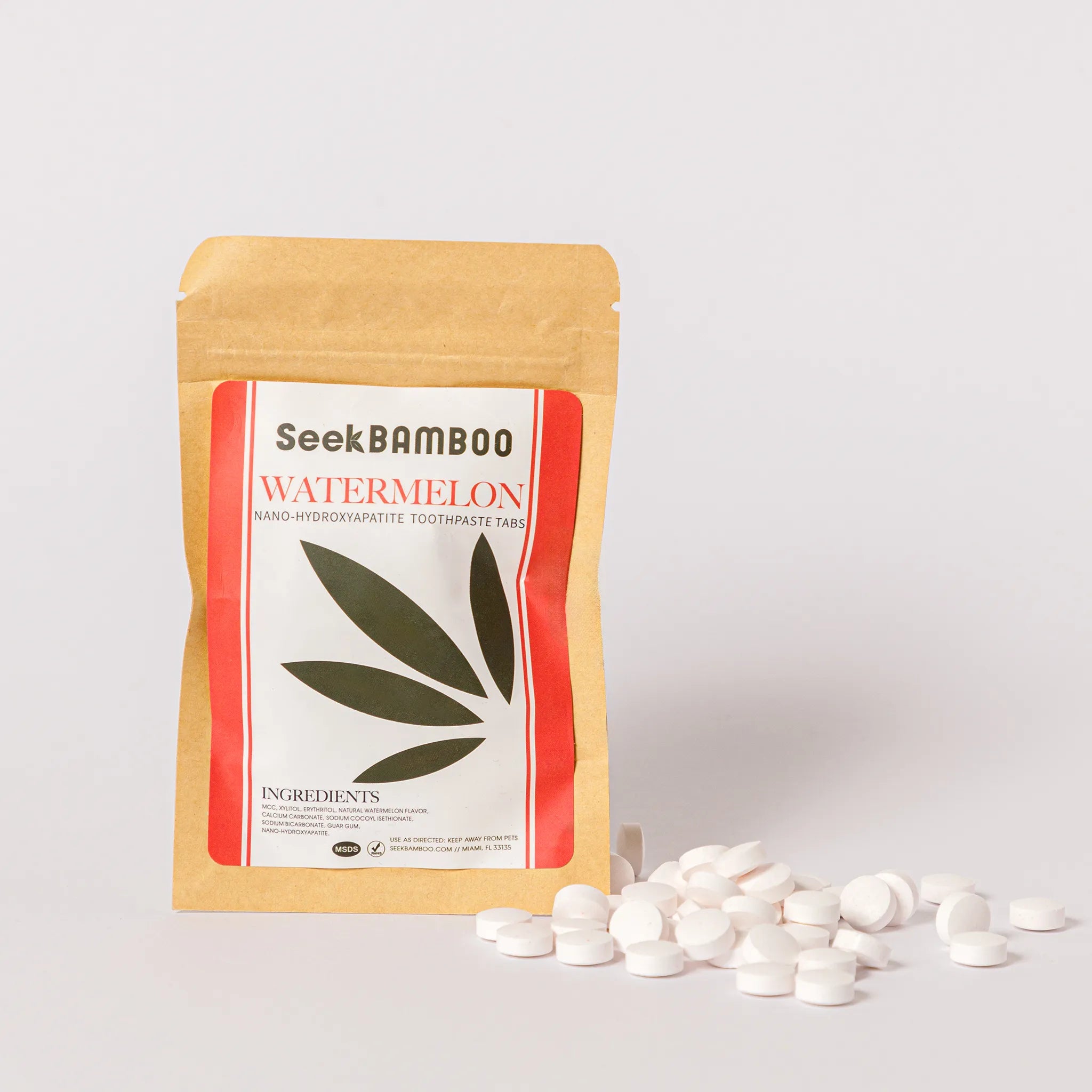 SeekBamboo Fluoride Free Watermelon toothpaste tablets in a kraft paper stand-up pouch with a white and red label, shown with several white round tablets scattered in front on a light gray background.