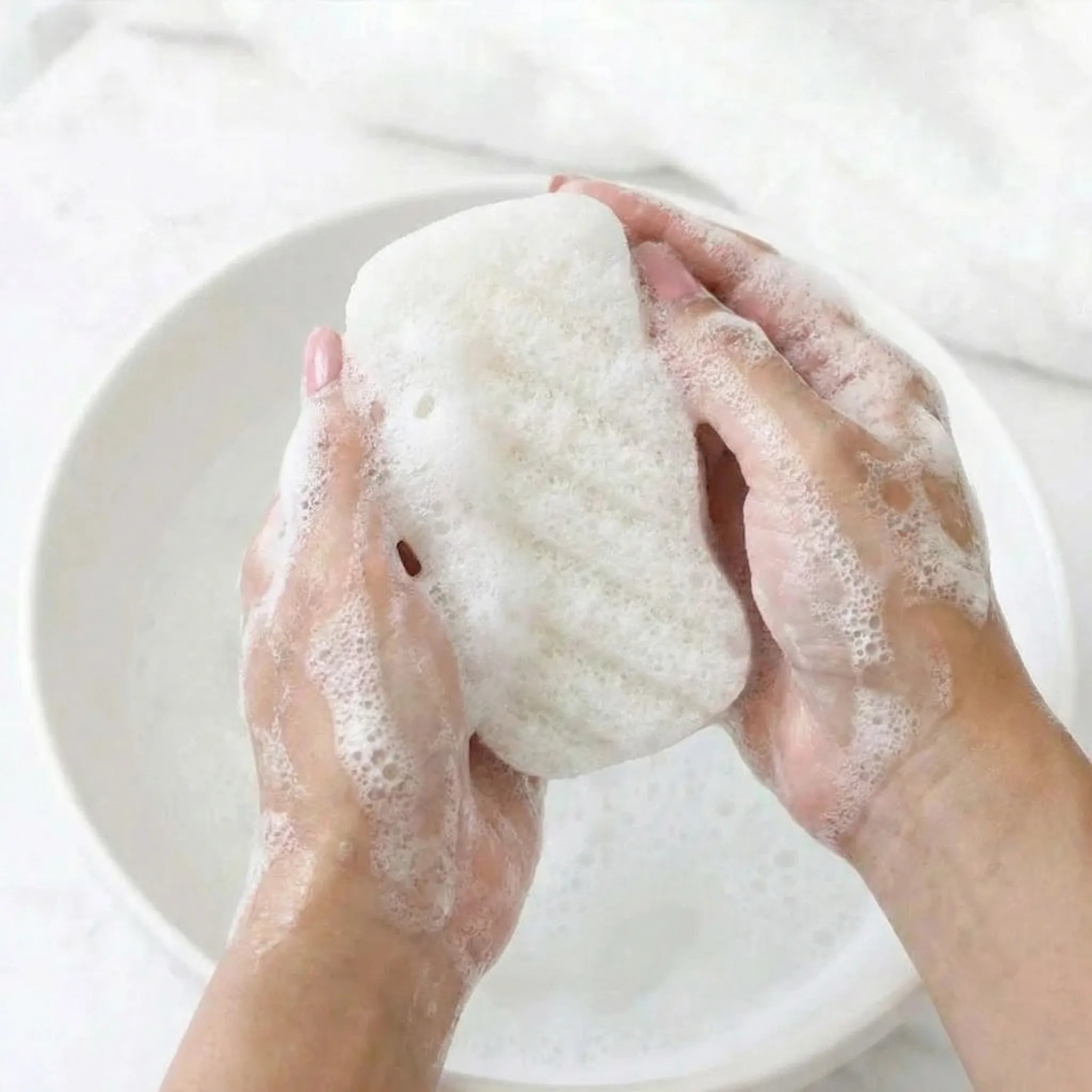 Foamy unscented konjac sponge held between hands with a blurred background