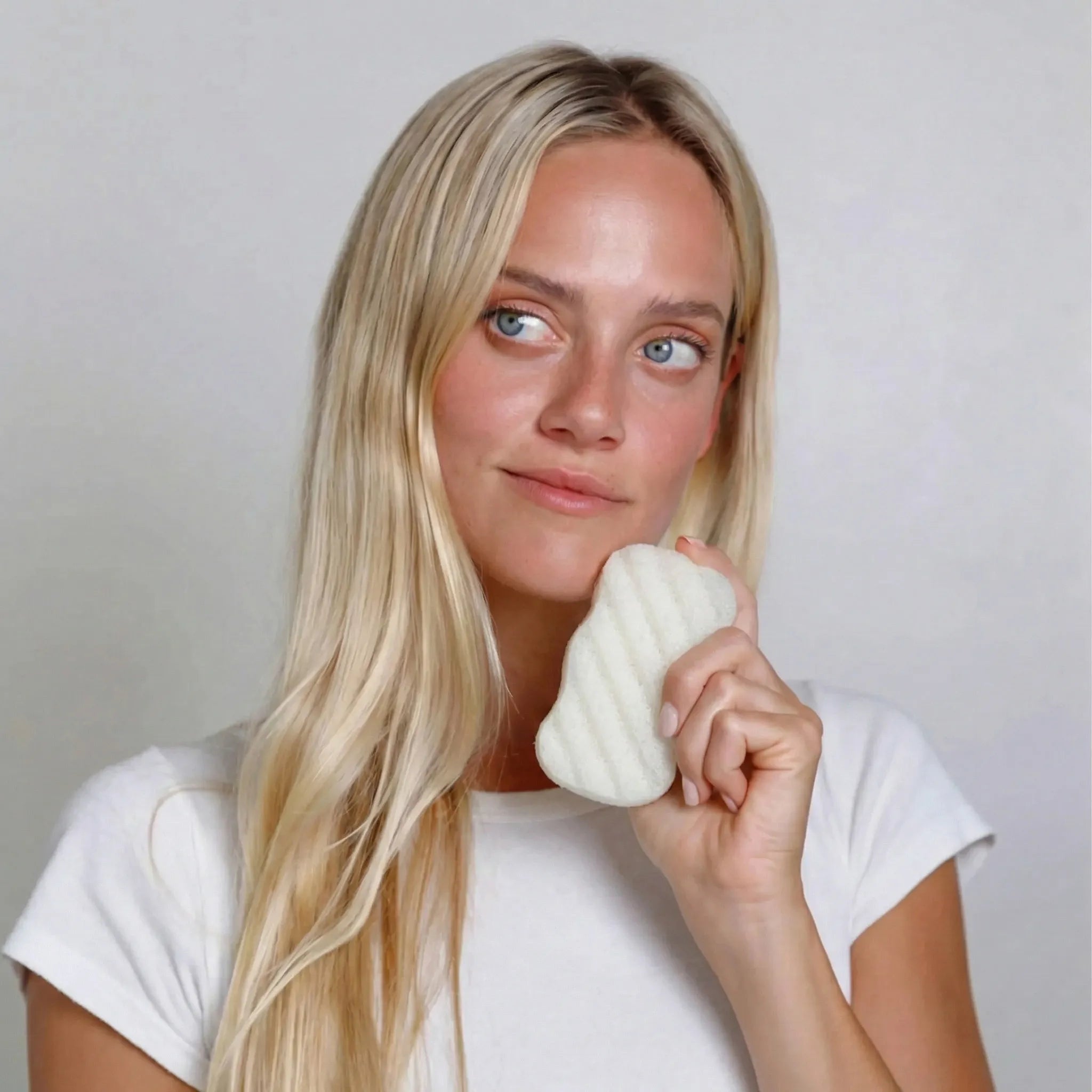 Woman holding a unscented body konjac sponge against a plain background