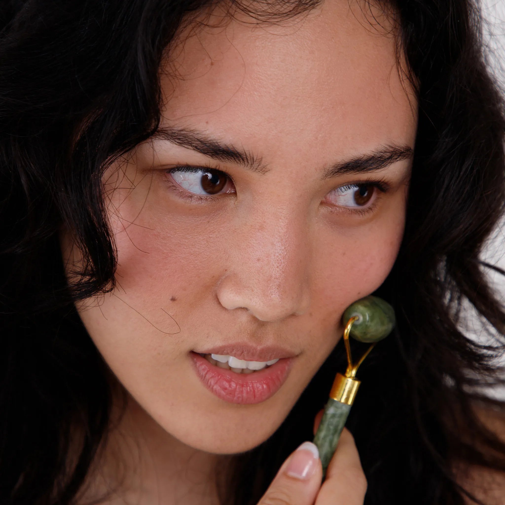 Woman using a green facial roller on her face