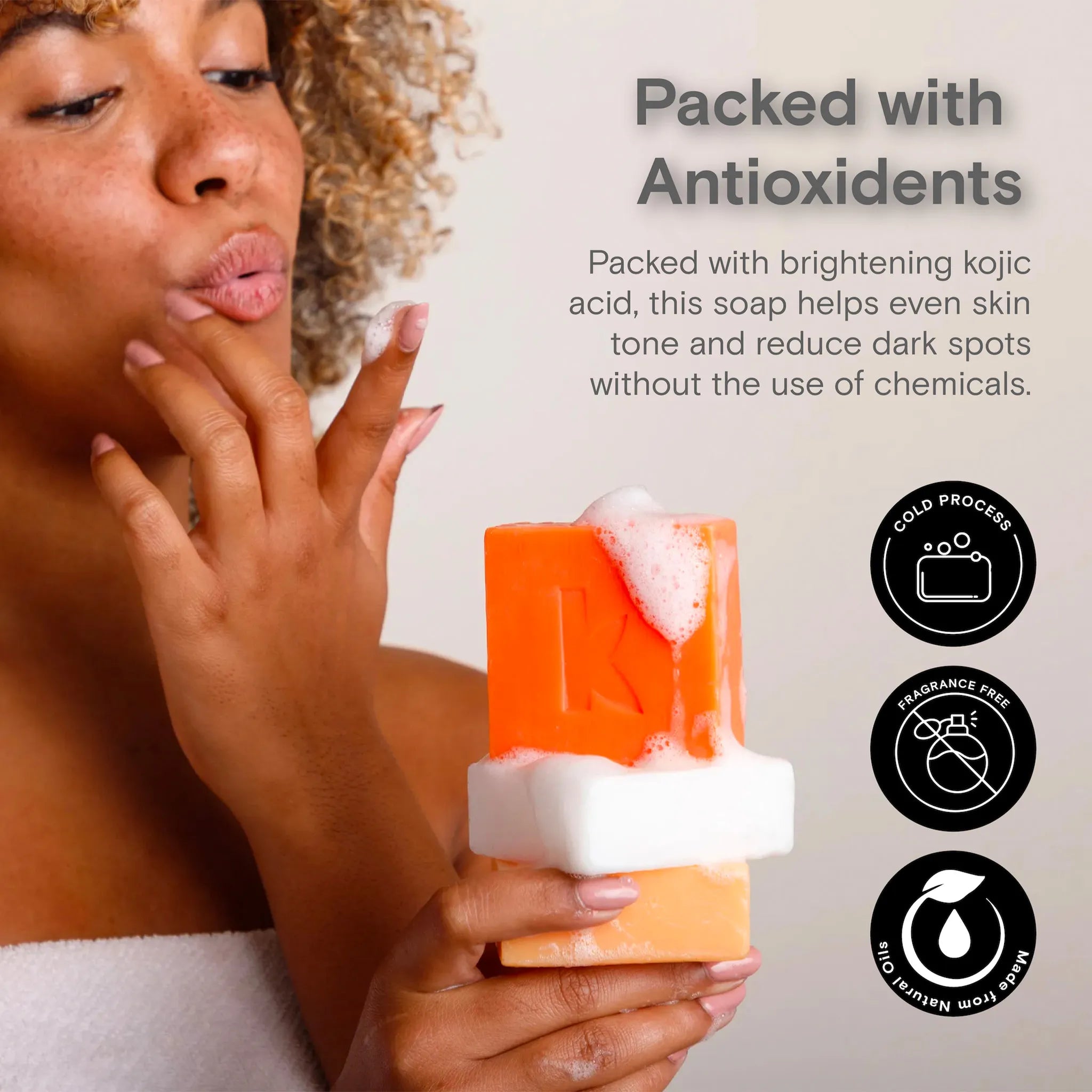 Person holding an orange soap bar with text about antioxidants and skin benefits.