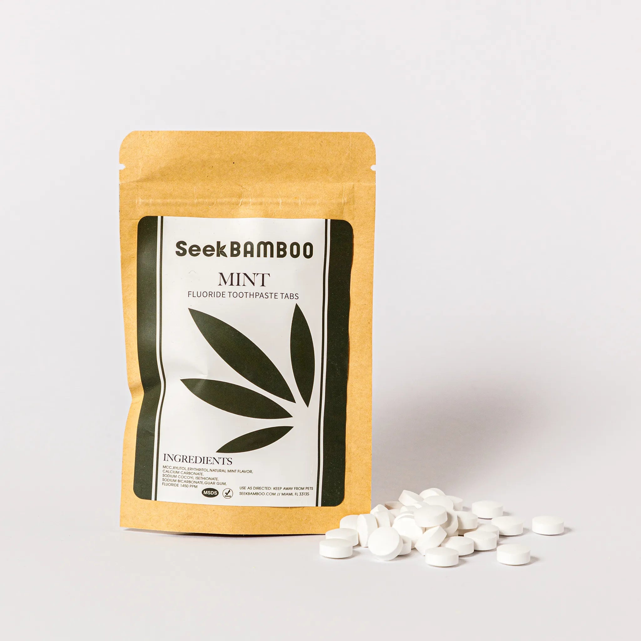 A kraft paper pouch of SeekBAMBOO Mint Fluoride Toothpaste Tabs stands on a white background with several white round tablets scattered in front.