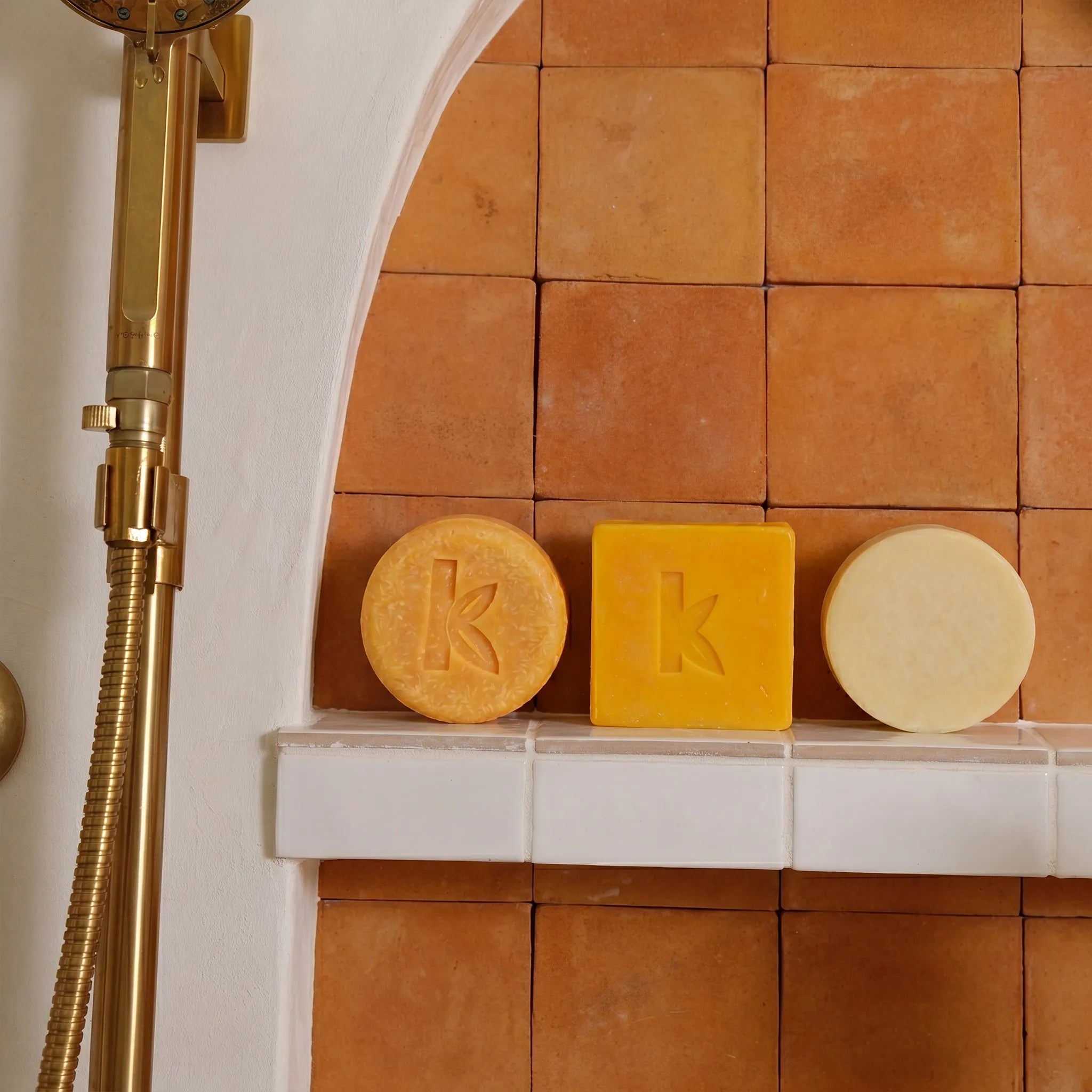 Ginger Shampoo, soap and conditioner on a white ledge against an orange tiled wall.