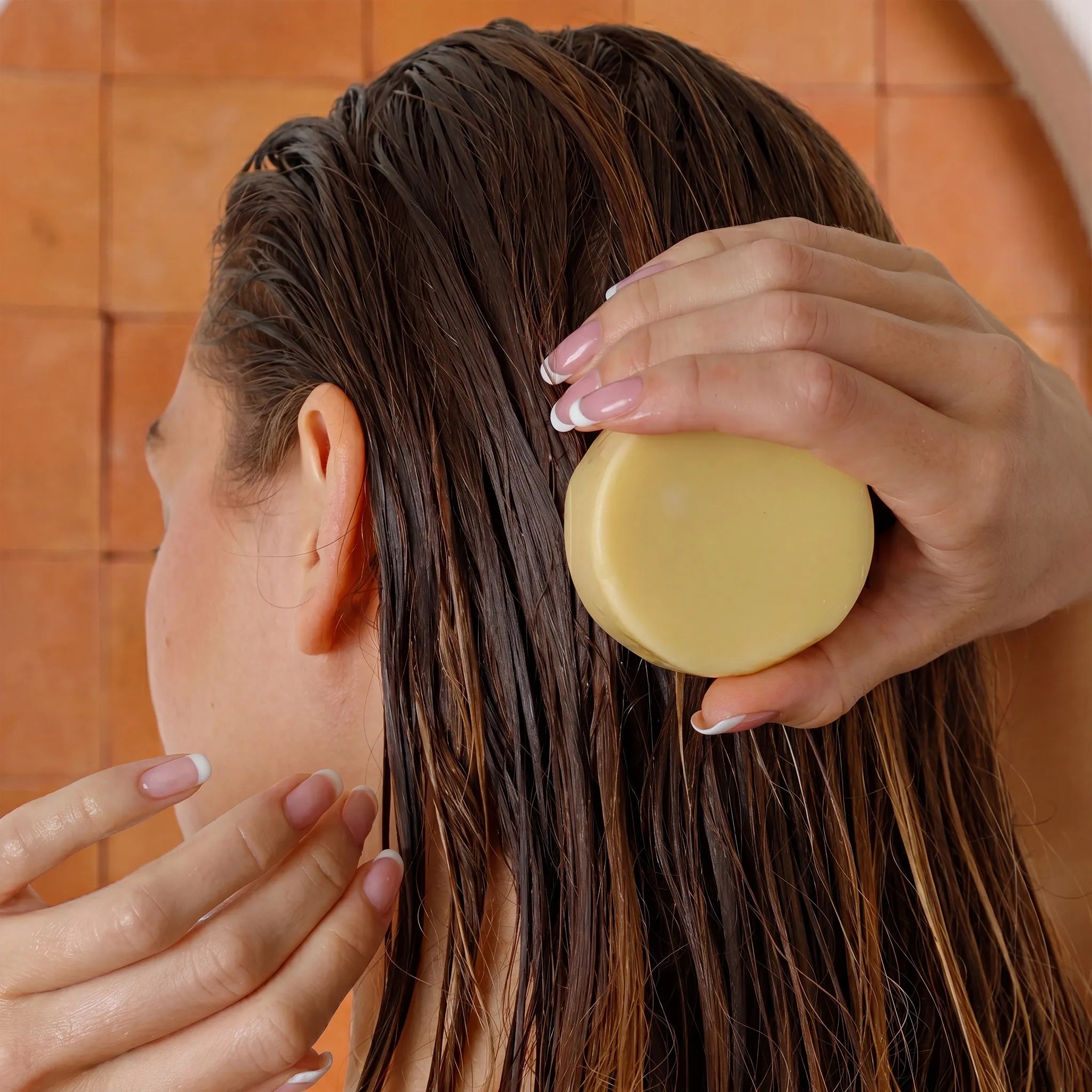 Person applying a ginger conditioner bar of soap to their hair in a bathroom setting.
