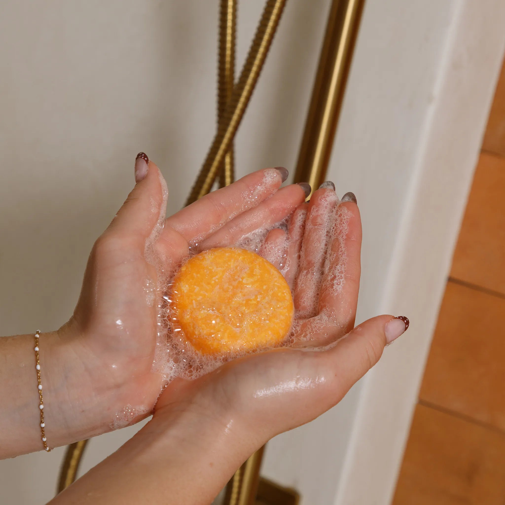 Hand holding a honey shampoo bar with soap suds in a bathroom setting