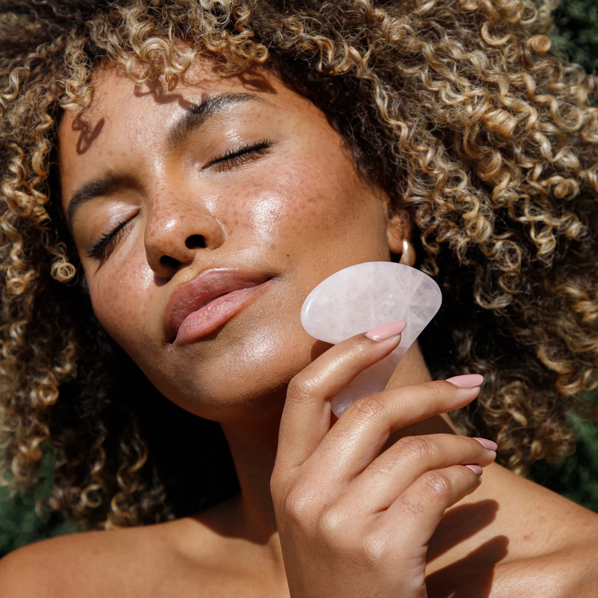 Woman using a rose quartz crystal on her face outdoors