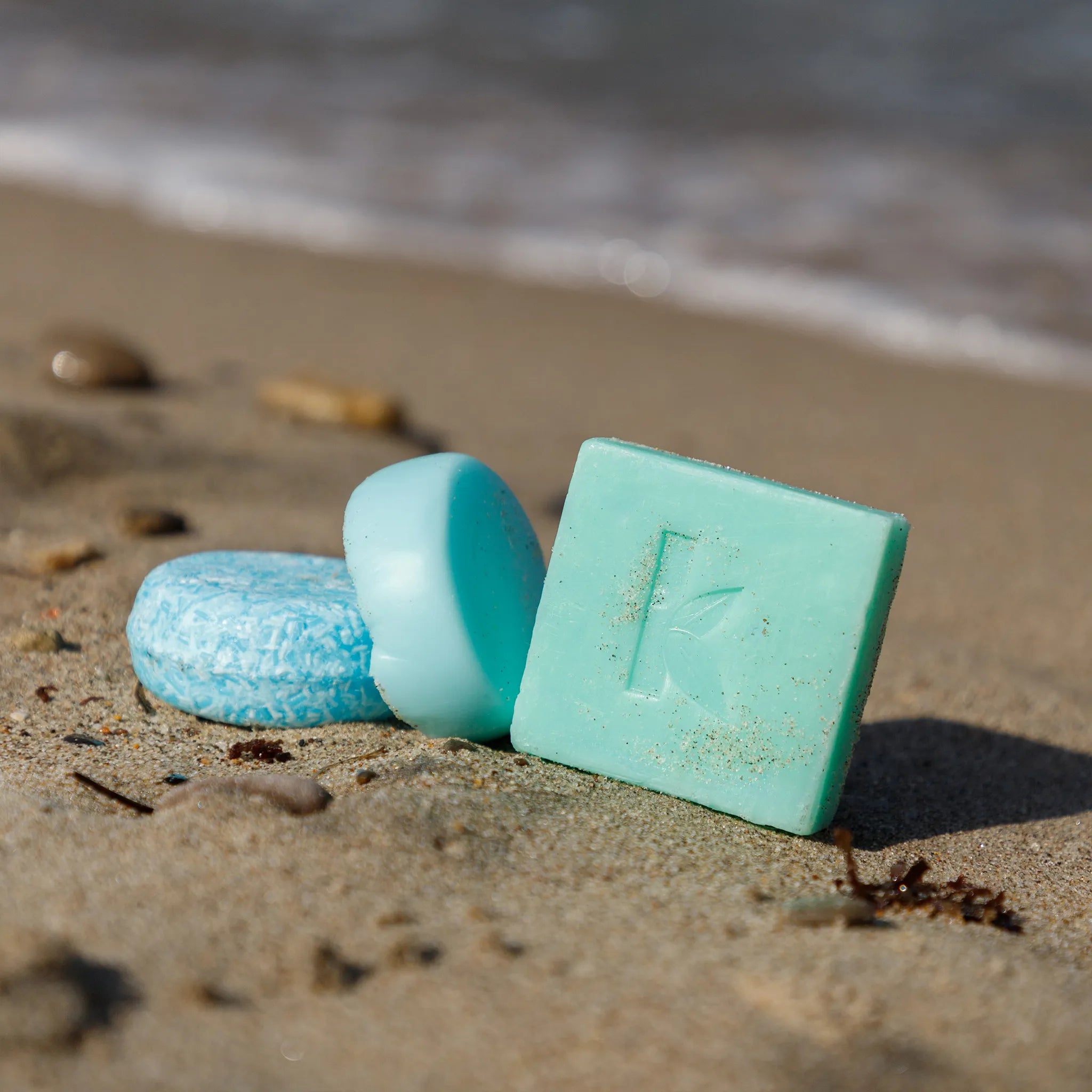 Three seaweed soaps on a sandy beach with ocean waves in the background.