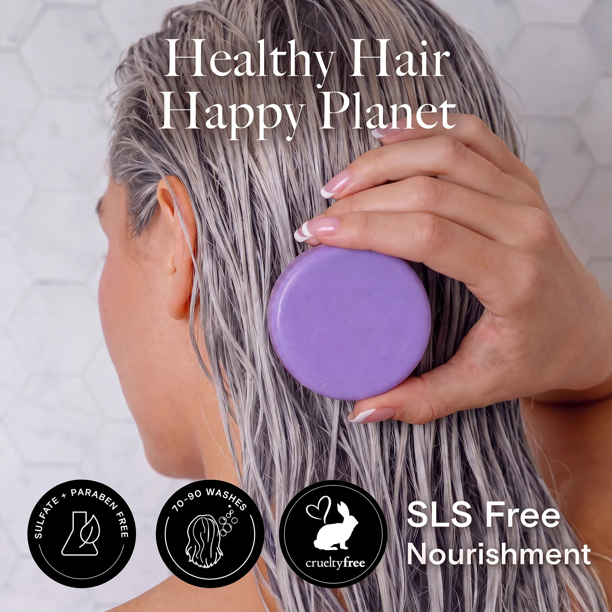 A person with wet gray hair holds a round purple conditioner bar against their head. Large text reads 'Healthy Hair Happy Planet,' with three black certification-style icons at the bottom and additional text reading 'SLS Free Nourishment.