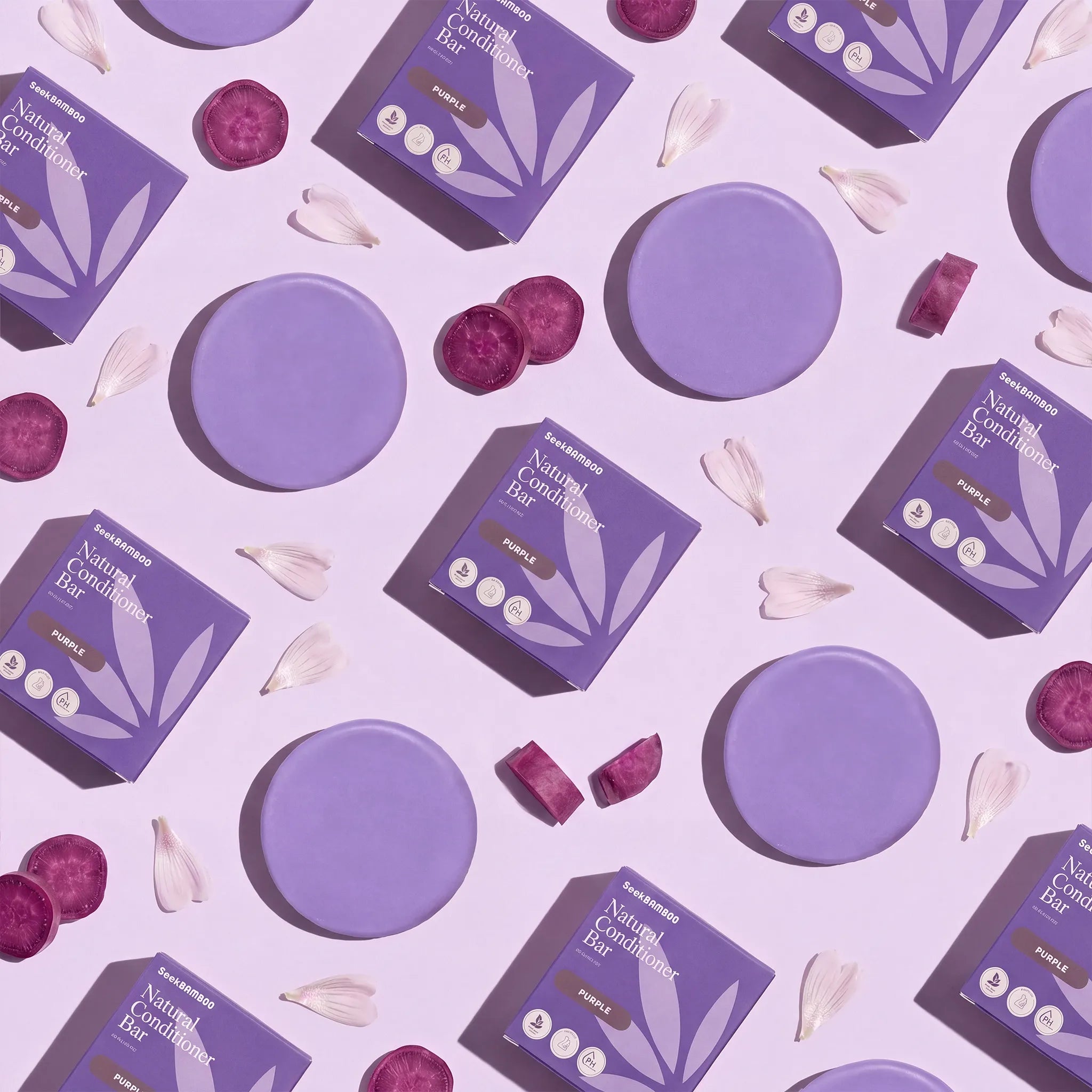A flat-lay arrangement of purple skincare packaging and circular purple product discs on a light lavender background, with scattered flower petals and a few dark purple slices. The boxes read 'Natural Beauty' and 'Peony'.