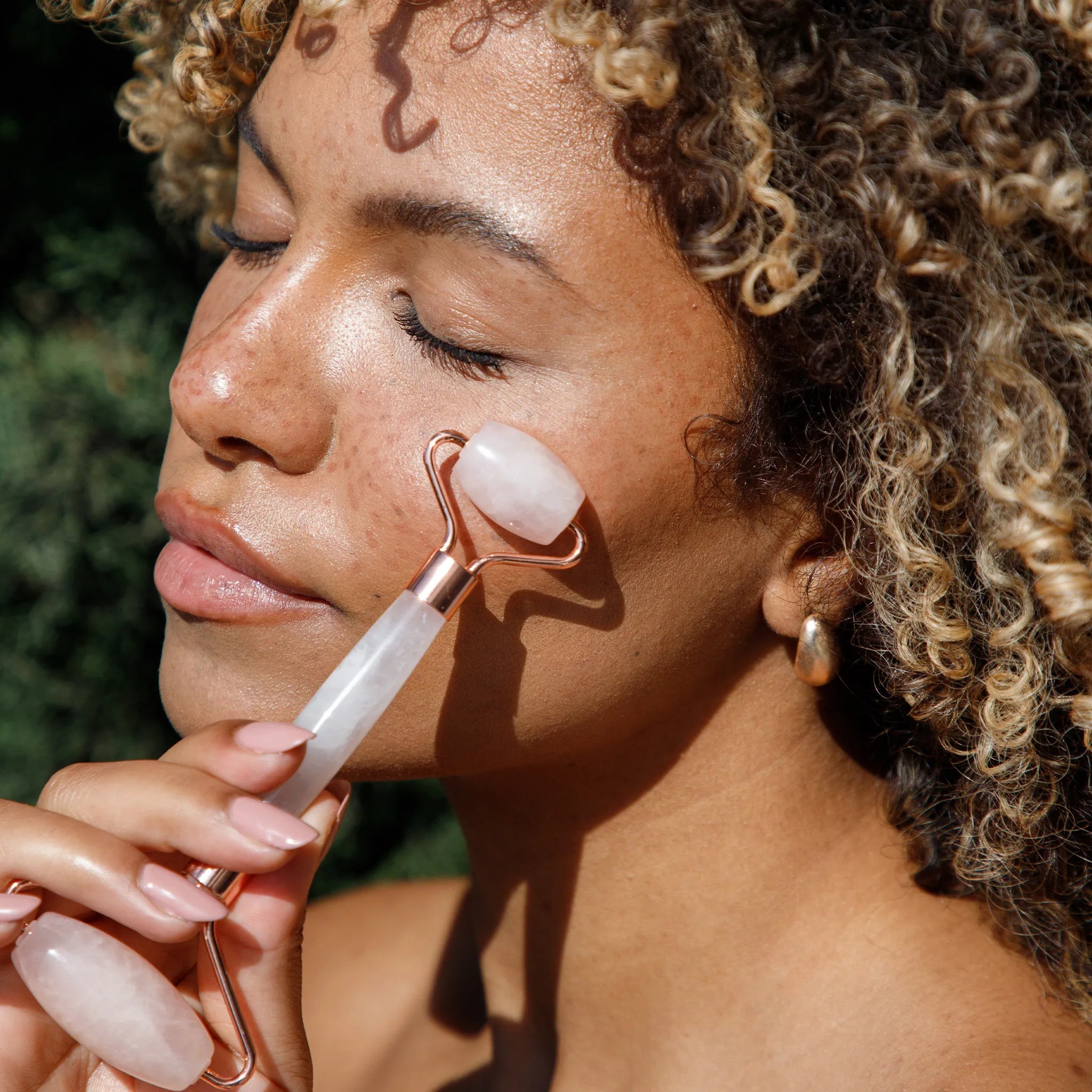 Woman using a rose quartz facial roller on her face with a blurred green background