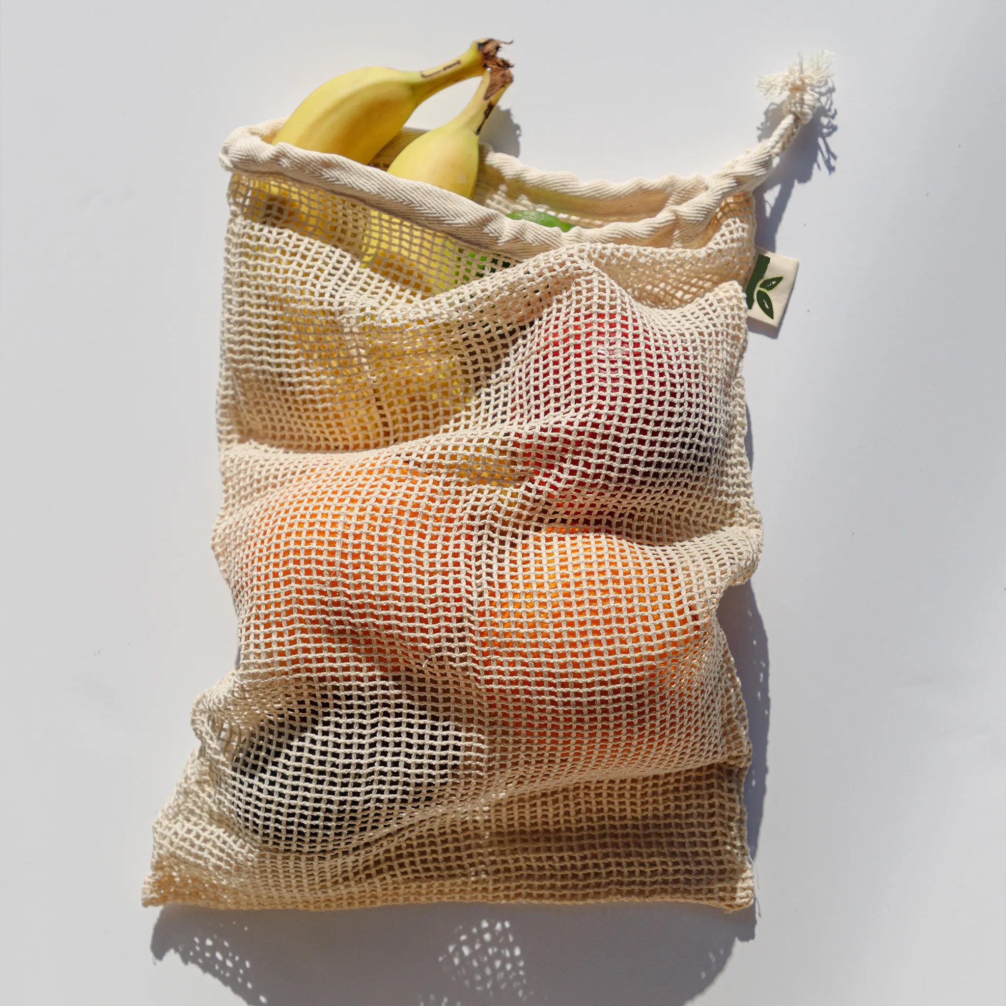 Mesh produce bag with fruits on a light gray background