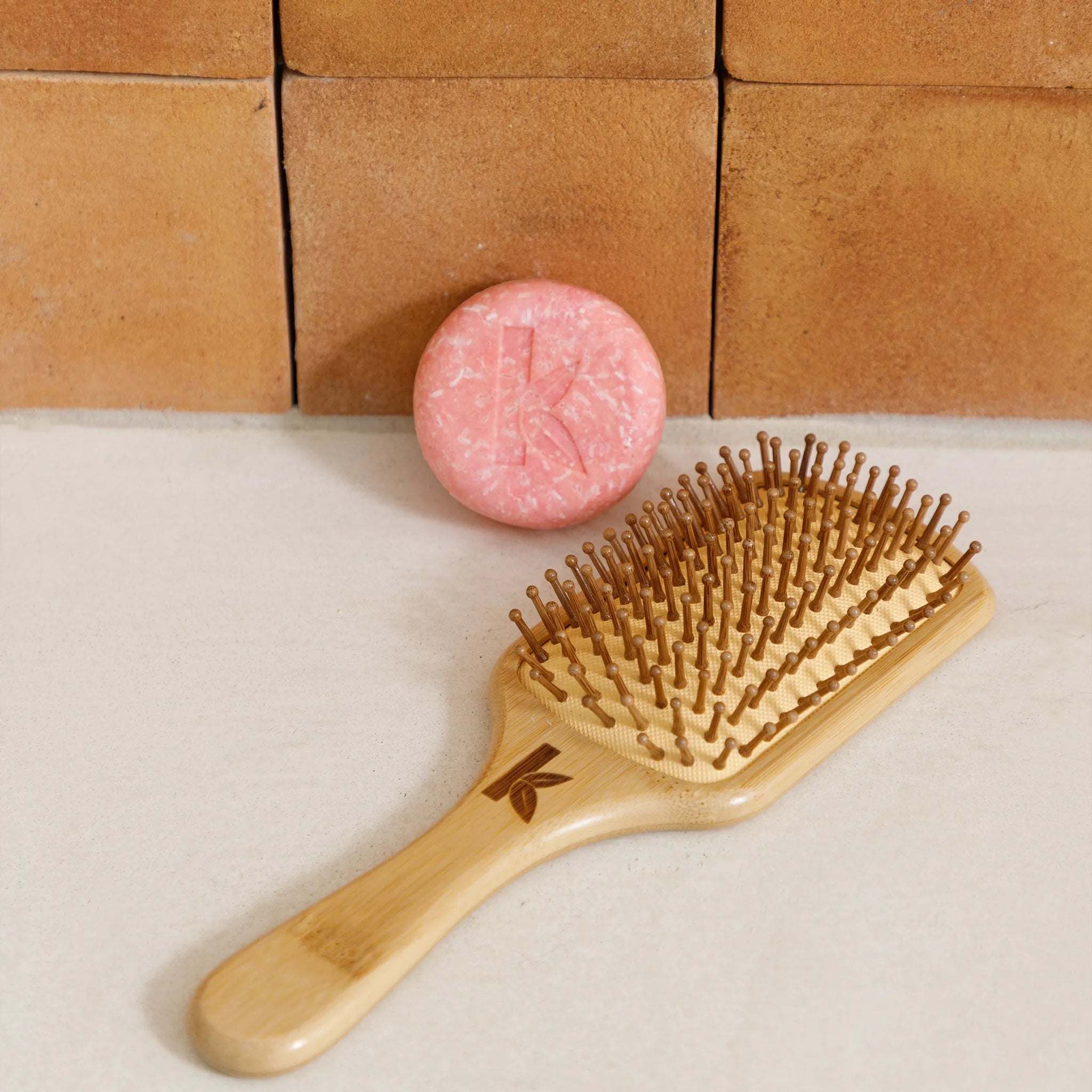 bamboo hairbrush and rose shampoo bar on a beige surface with a wooden block background