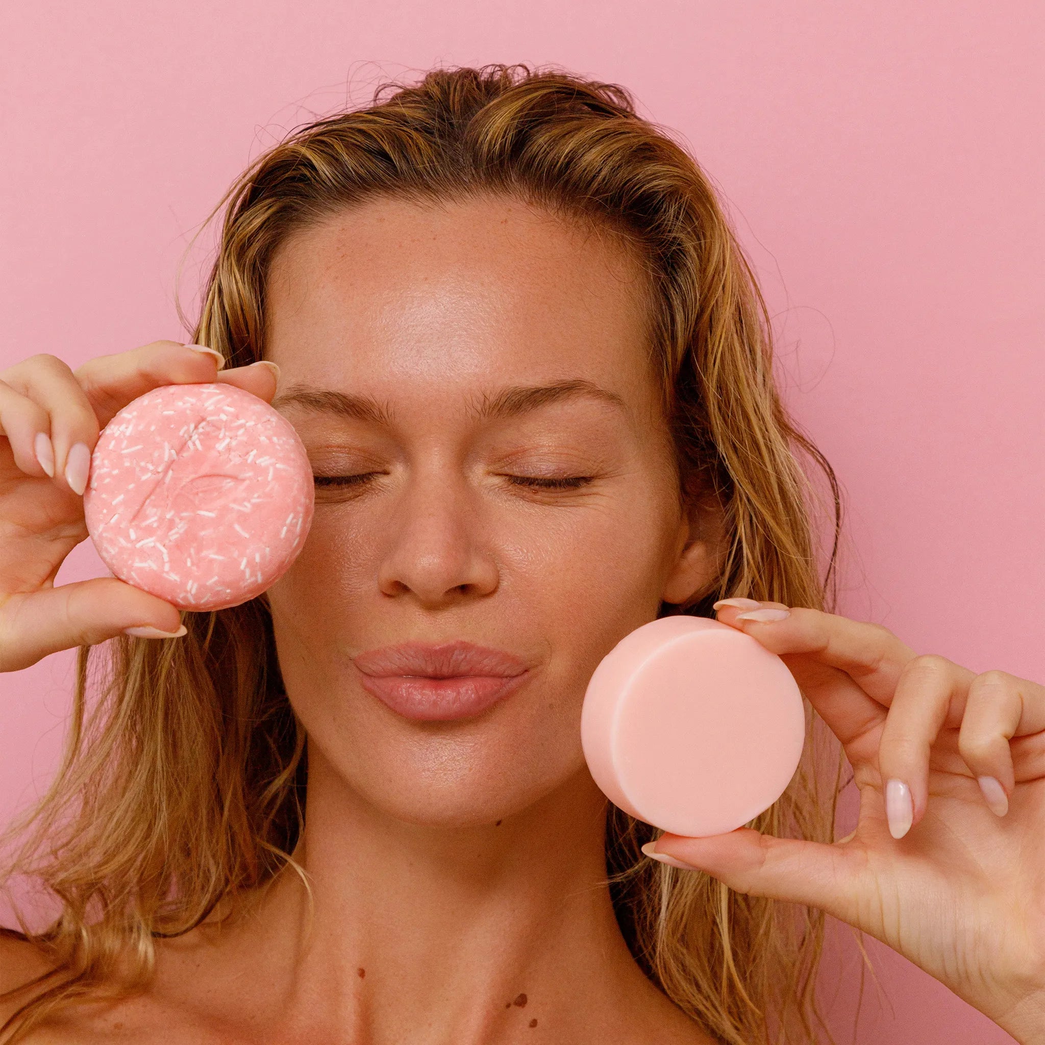 Woman holding a rose shampoo and conditioner against a pink background
