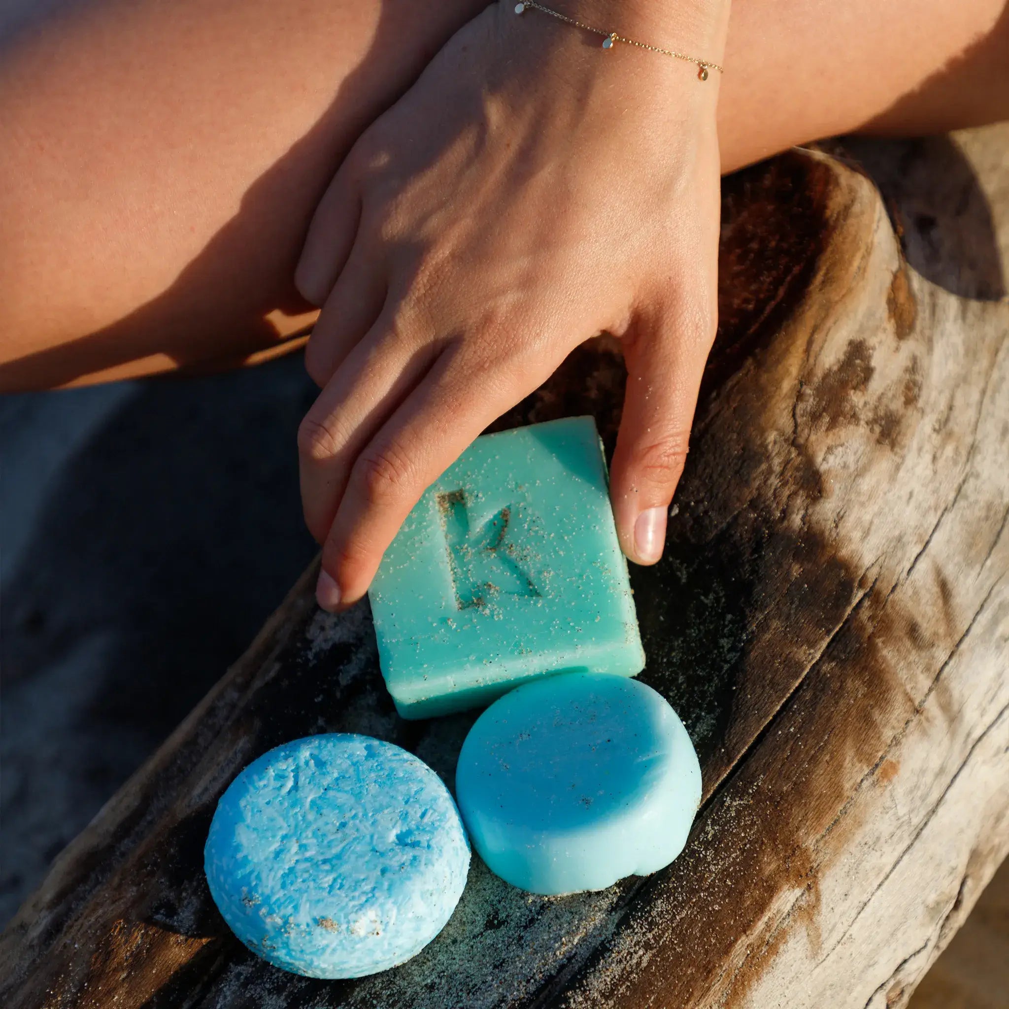 Hand holding a sea salt soap on a wooden surface with water in the background
