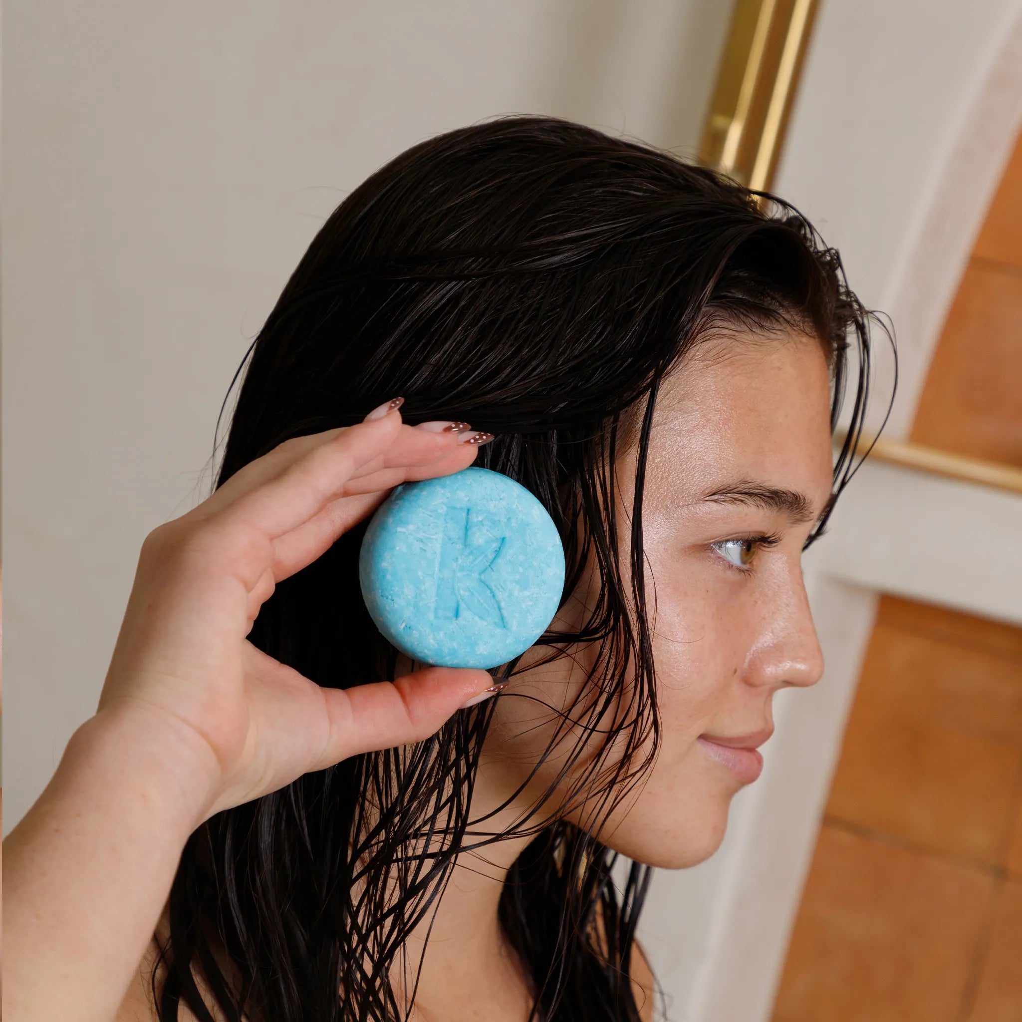 Person holding a seaweed shampoo bar with 'K' branding near their wet hair.