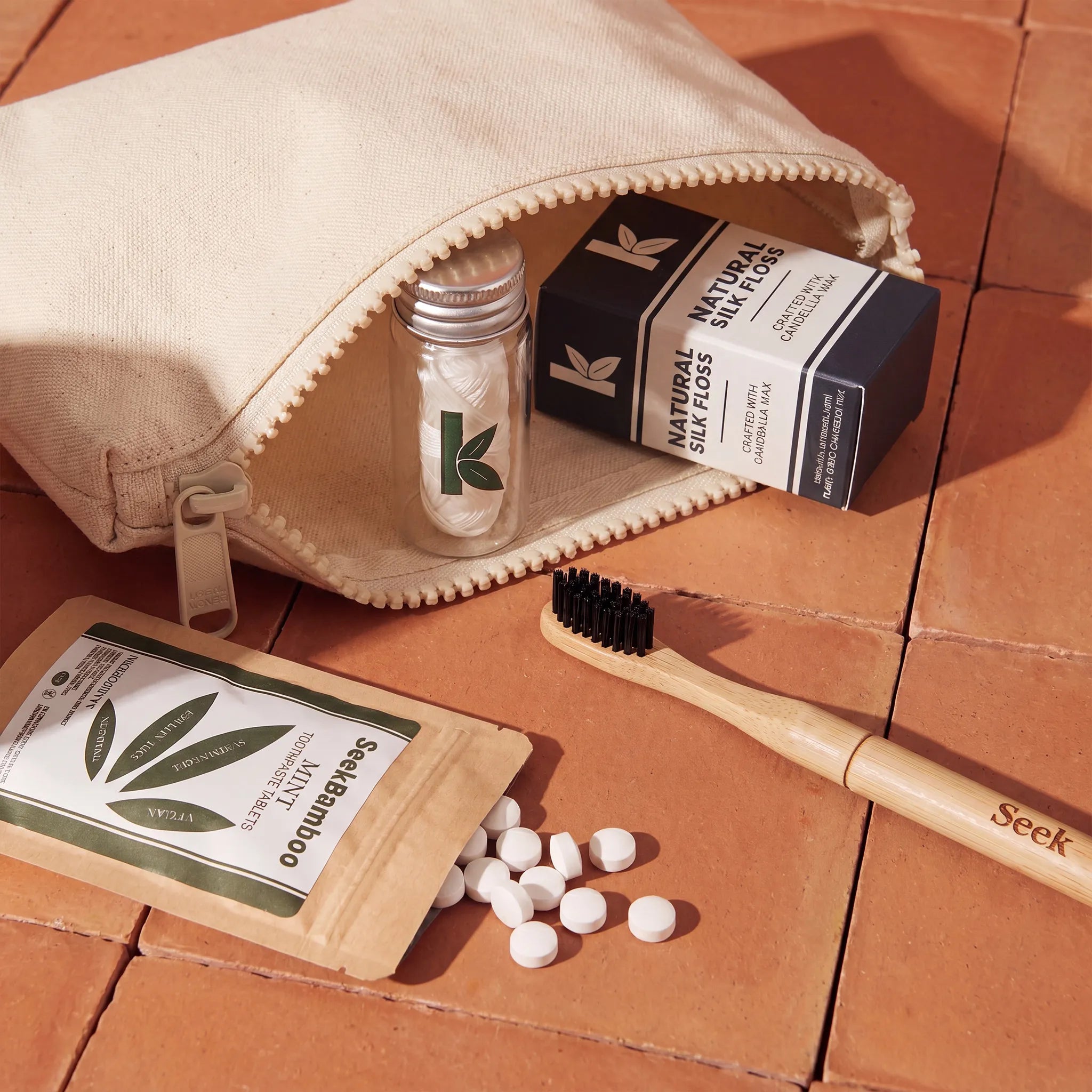 Toothbrush, dental floss, and toothpaste tablets on a terracotta surface with a beige bag.