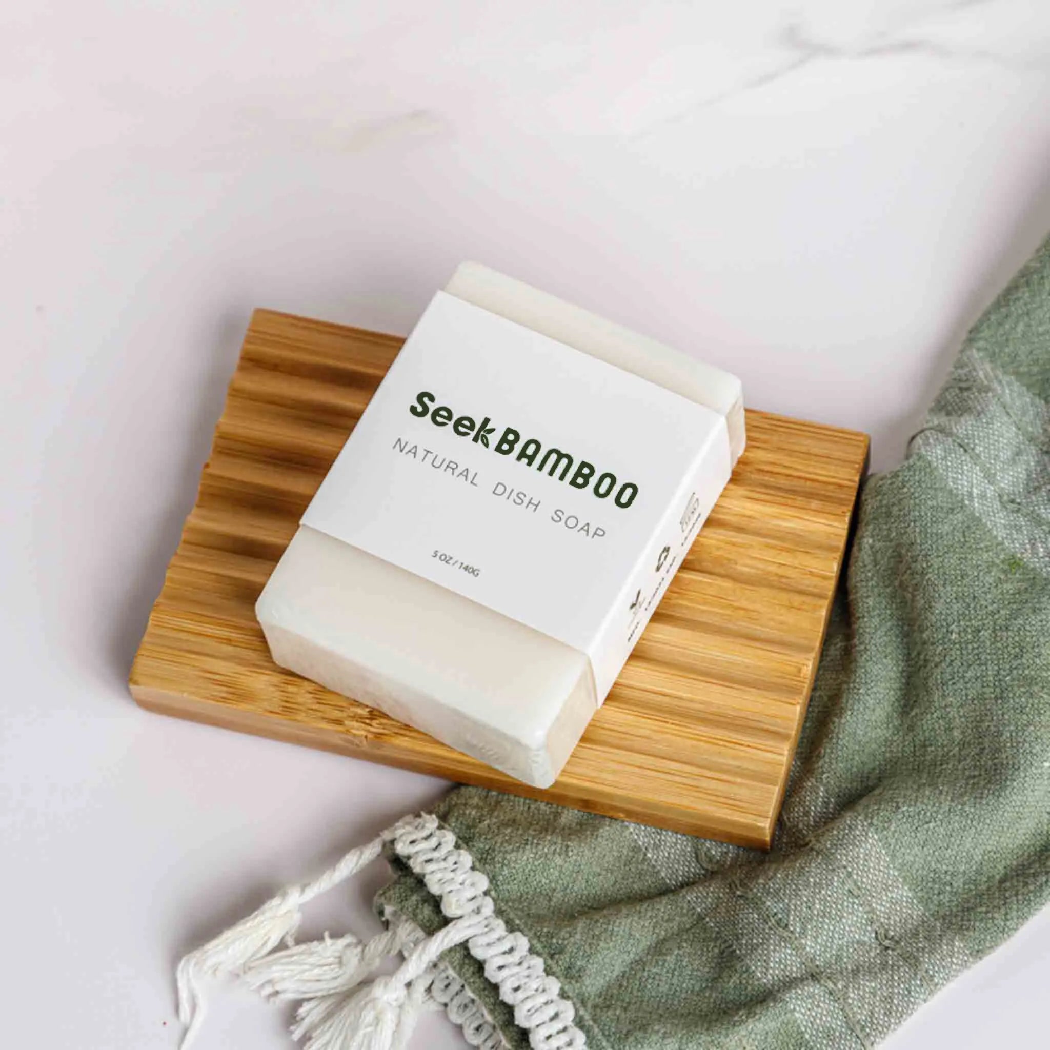 Bar of Seek Bamboo natural dish soap on a wooden soap dish with a green towel in the background.