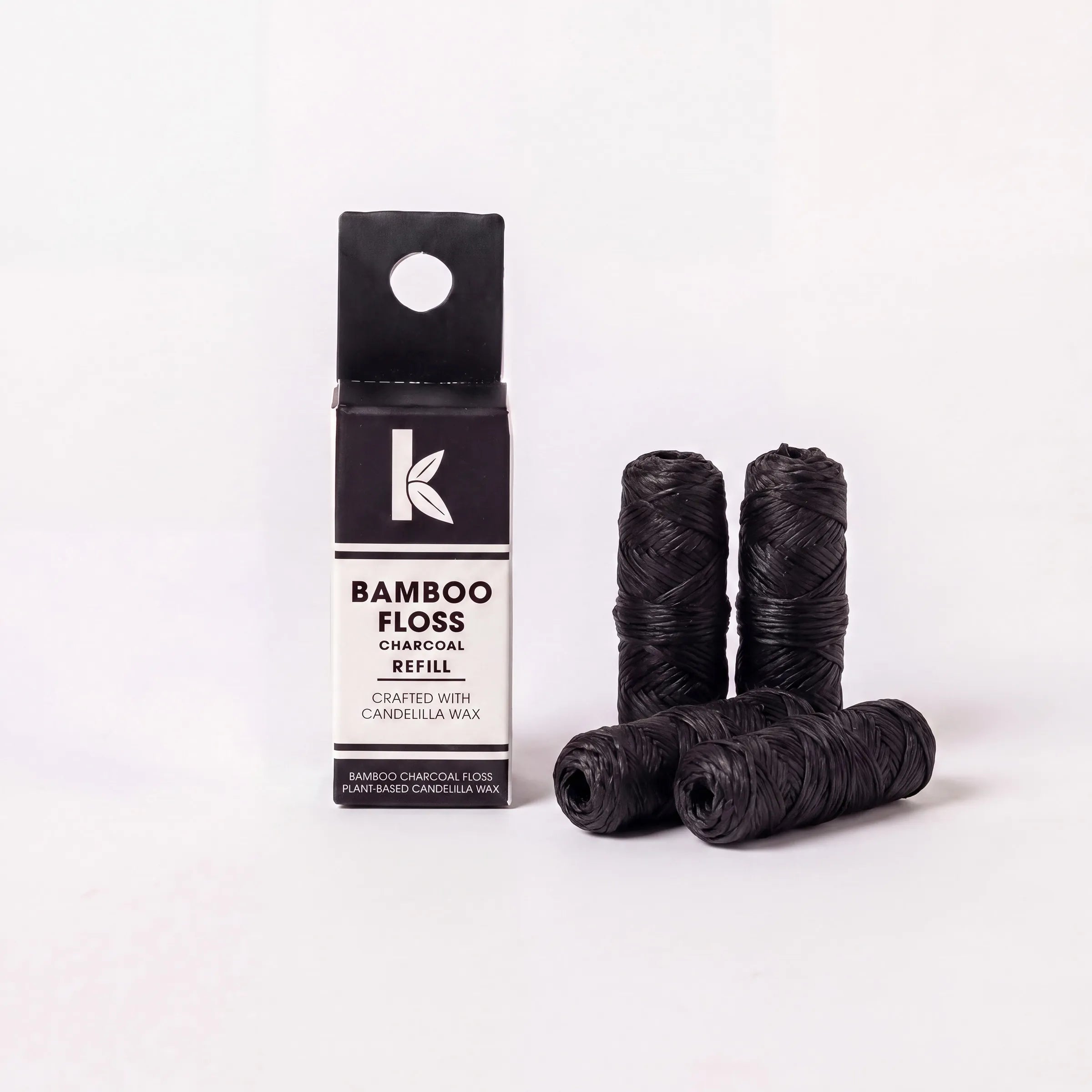 Bamboo Floss Charcoal Wax Refill containing four wound black thread spools next to their black and white cardboard packaging box on a clean white background.