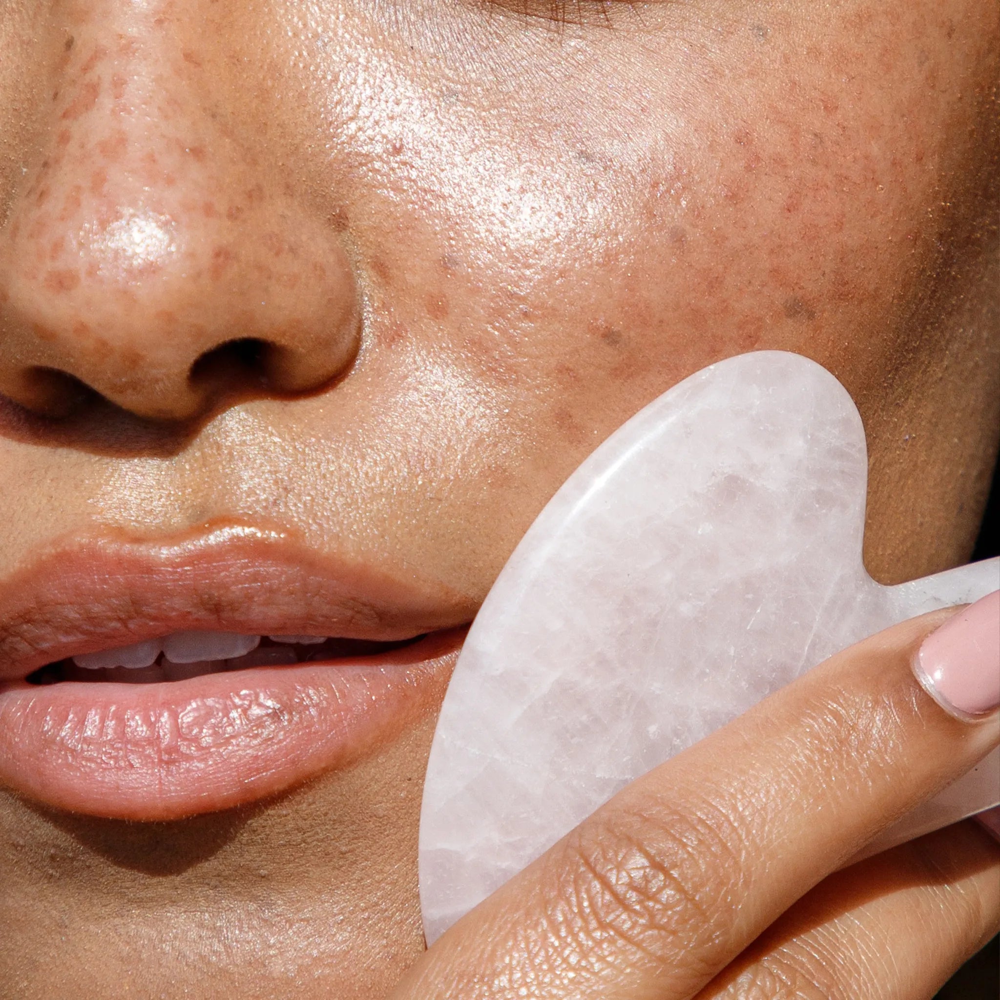 Close-up of a person using a white rose quartz roller on their face.