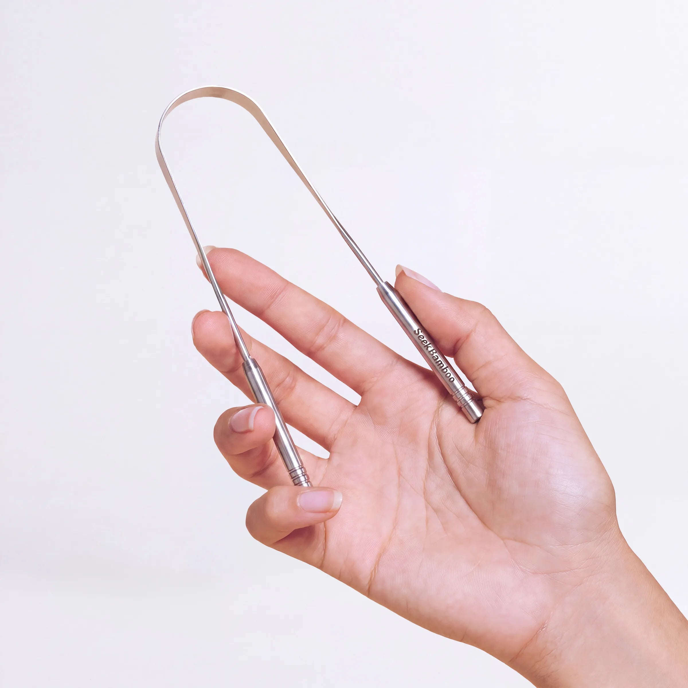 A hand holding a slim stainless steel seek bamboo tongue scrapper tool.