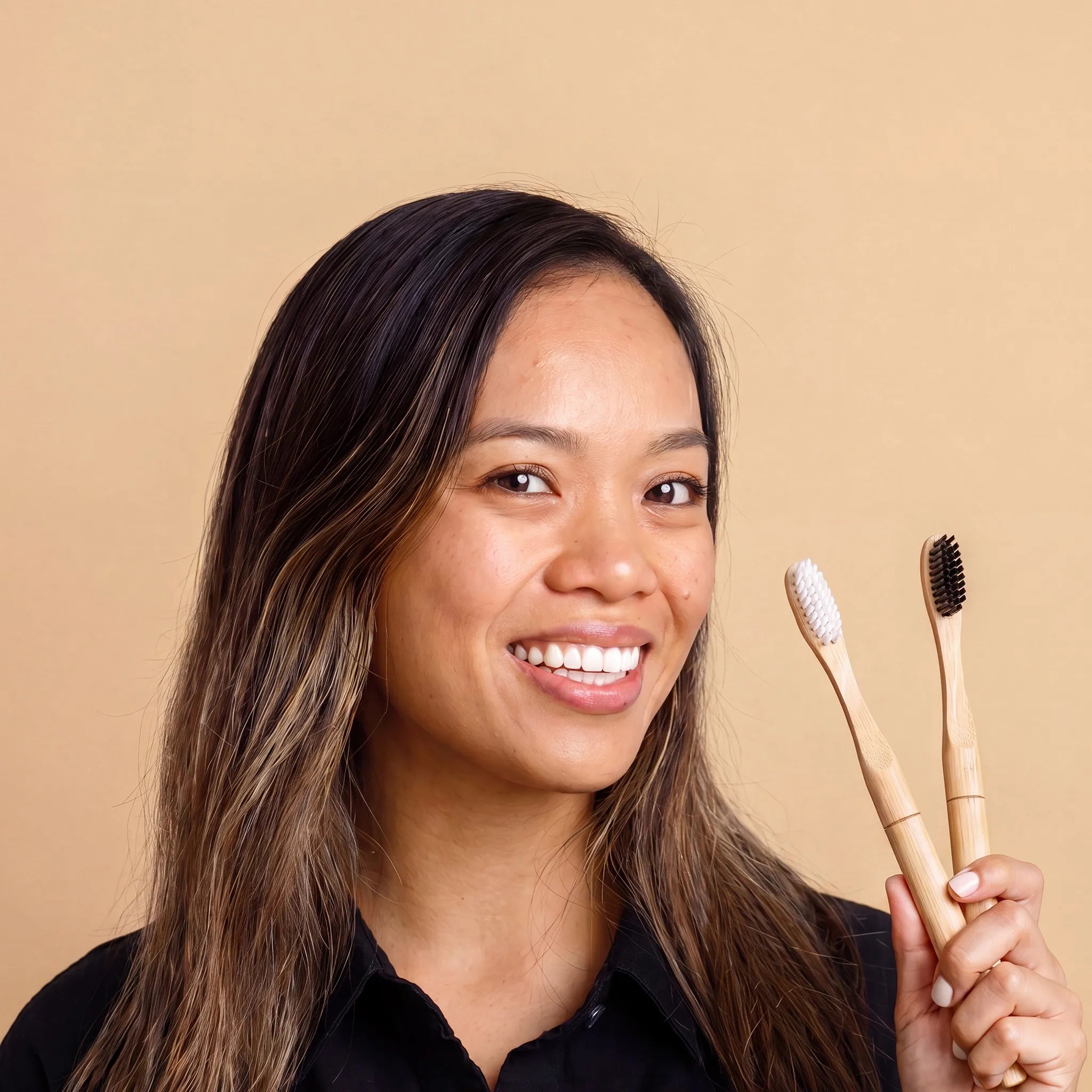 Woman holding two bamboo toothbrushes against a beige background