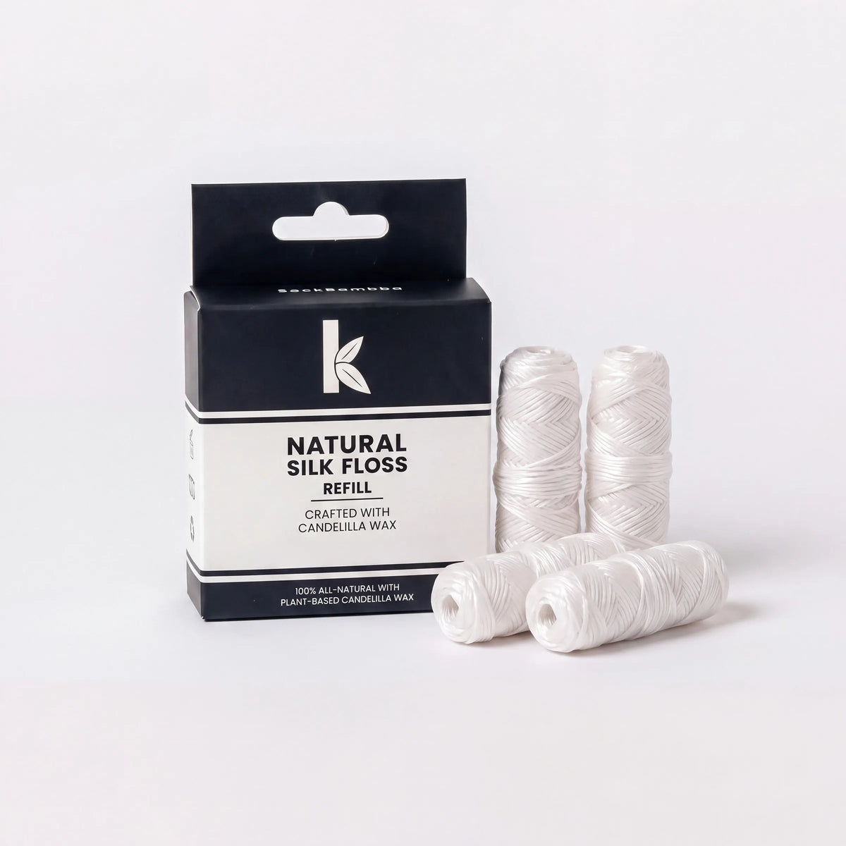 A package of Koda Natural Silk Floss Refill next to four spools of white thread on a clean white background.