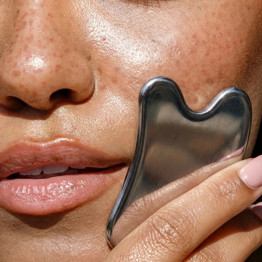 Close-up of a hand holding a stainless steel gua sha tool against a person's skin.