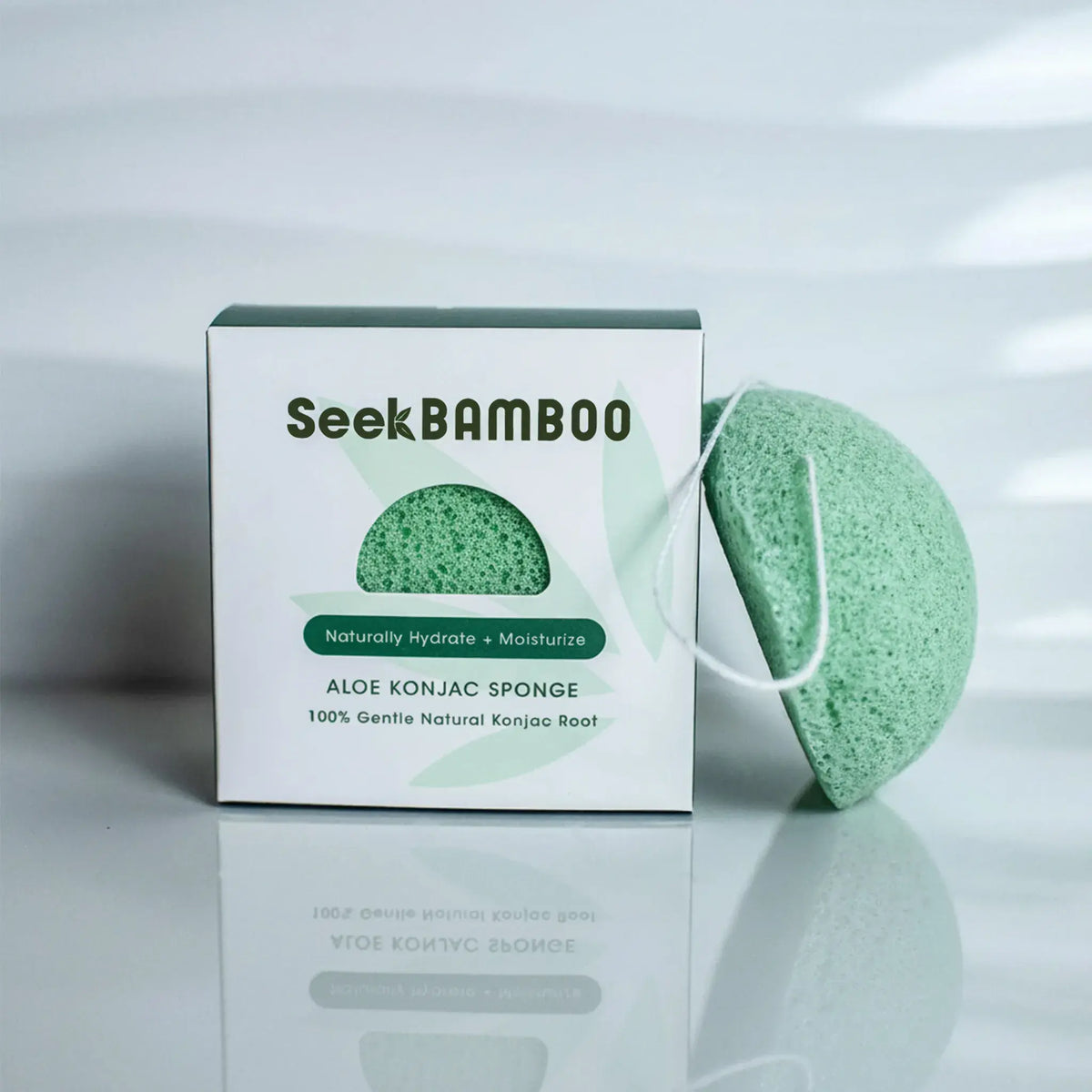 An aloe konjac sponge beside its packaging, with the brand name Seek Bamboo visible on the box. The sponge is green in color and made of natural konjac root fibers.