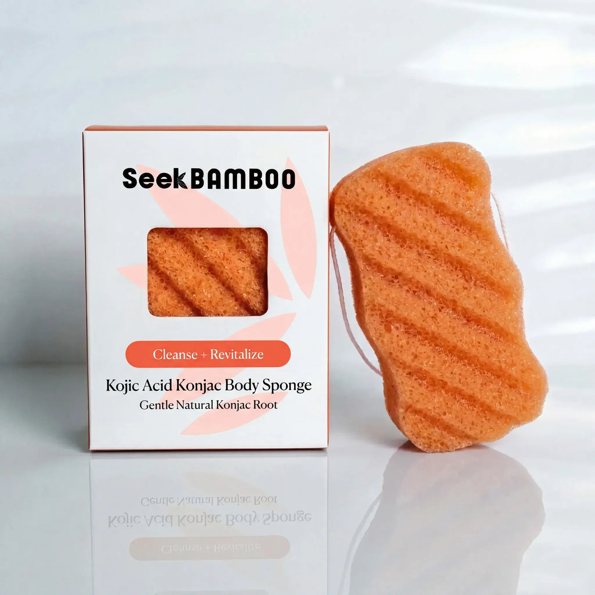 A Seek Bamboo kojic acid konjac body sponge in orange, shown next to its white and orange packaging box on a reflective white surface.