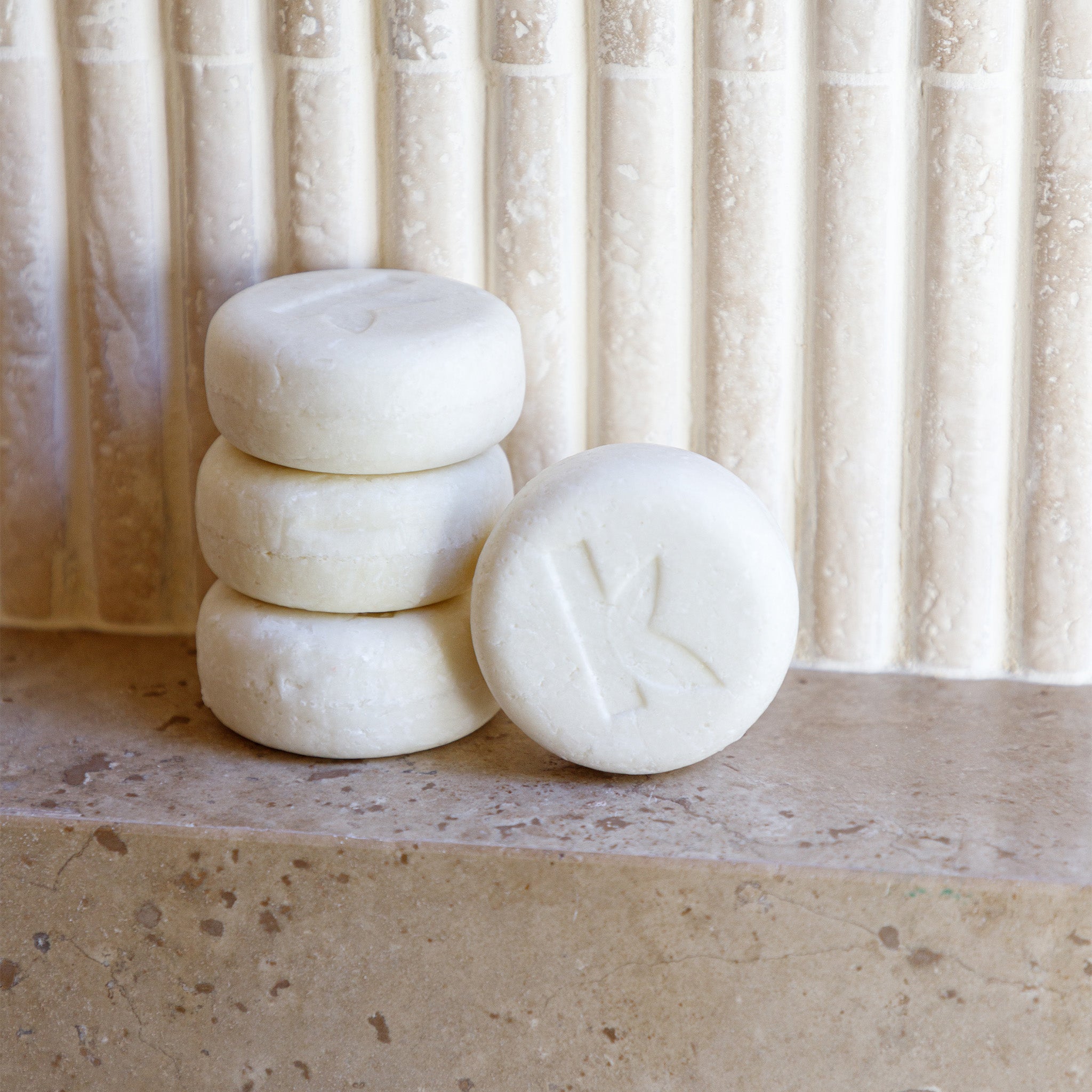 Three rice water shampoo bars stacked on a stone surface with a neutral curtain background