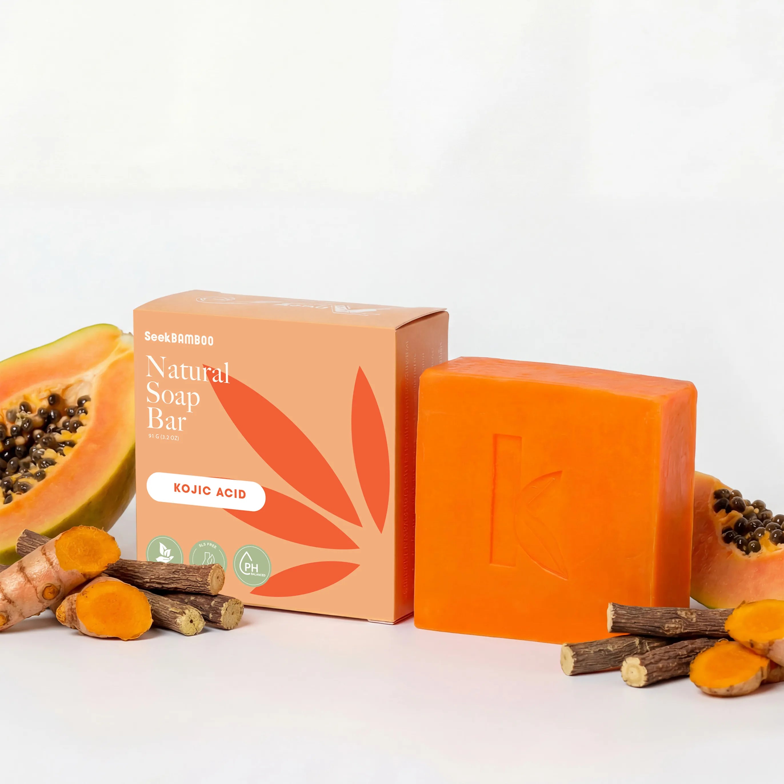 A bar of brightening soap powered by koijic acid is displayed on a white surface, styled with fresh turmeric roots and sliced papayas.