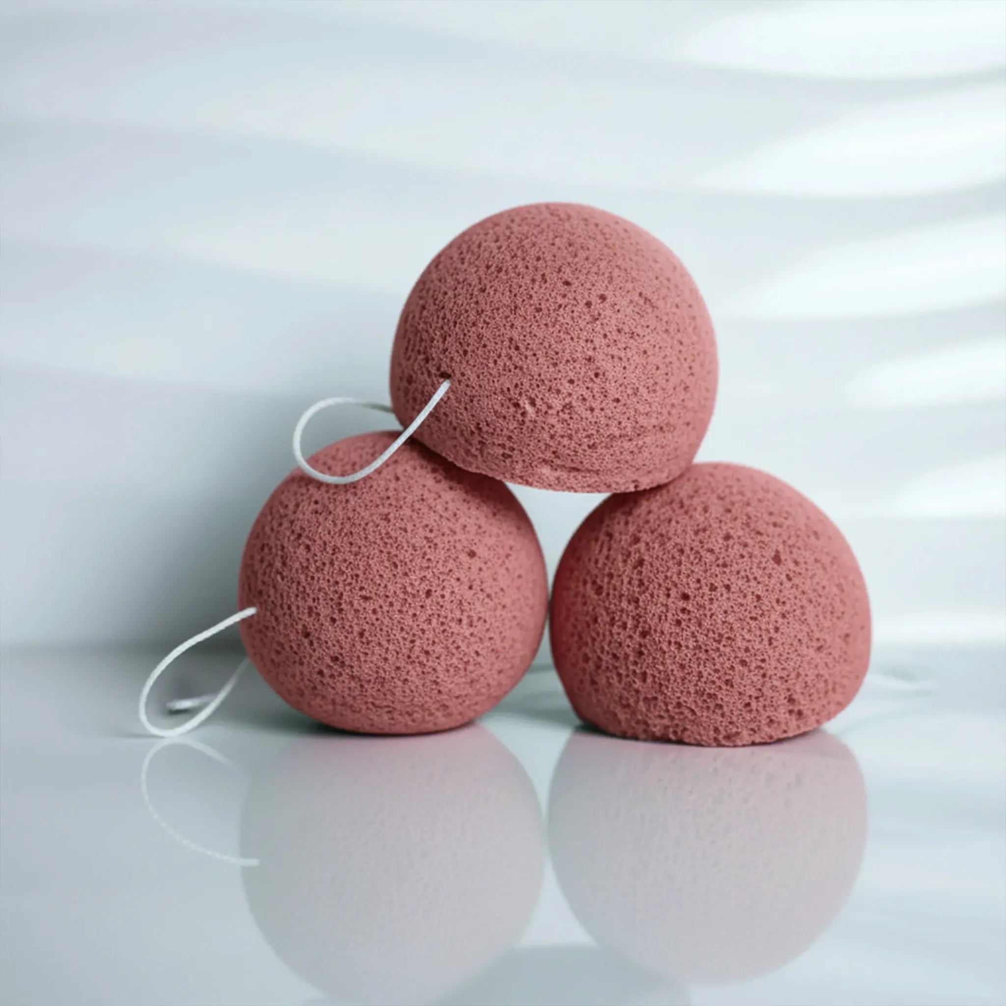 Three red clay konjac sponges stacked on a reflective surface with a white background