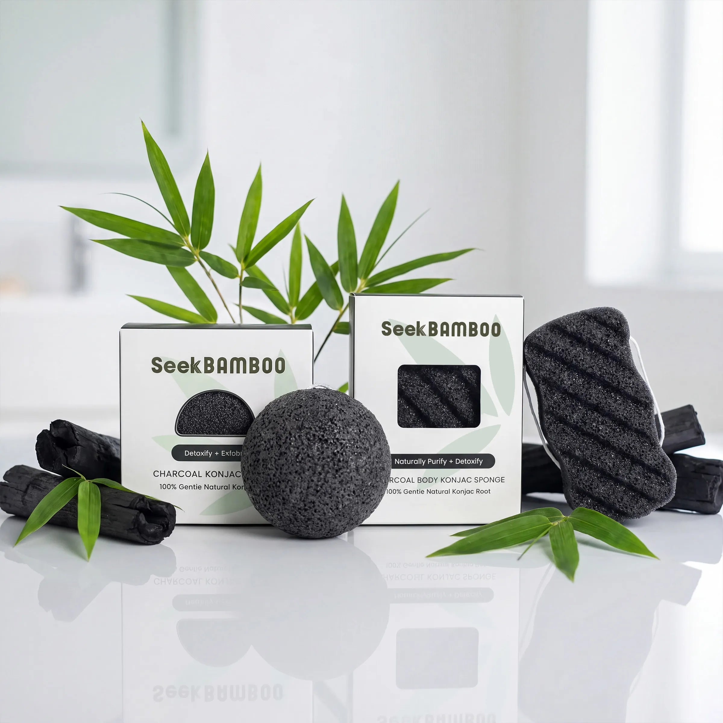 Two boxes of Seek Bamboo charcoal body purifying sponge along with two black sponge pads and bamboo leaves on a reflective white surface.