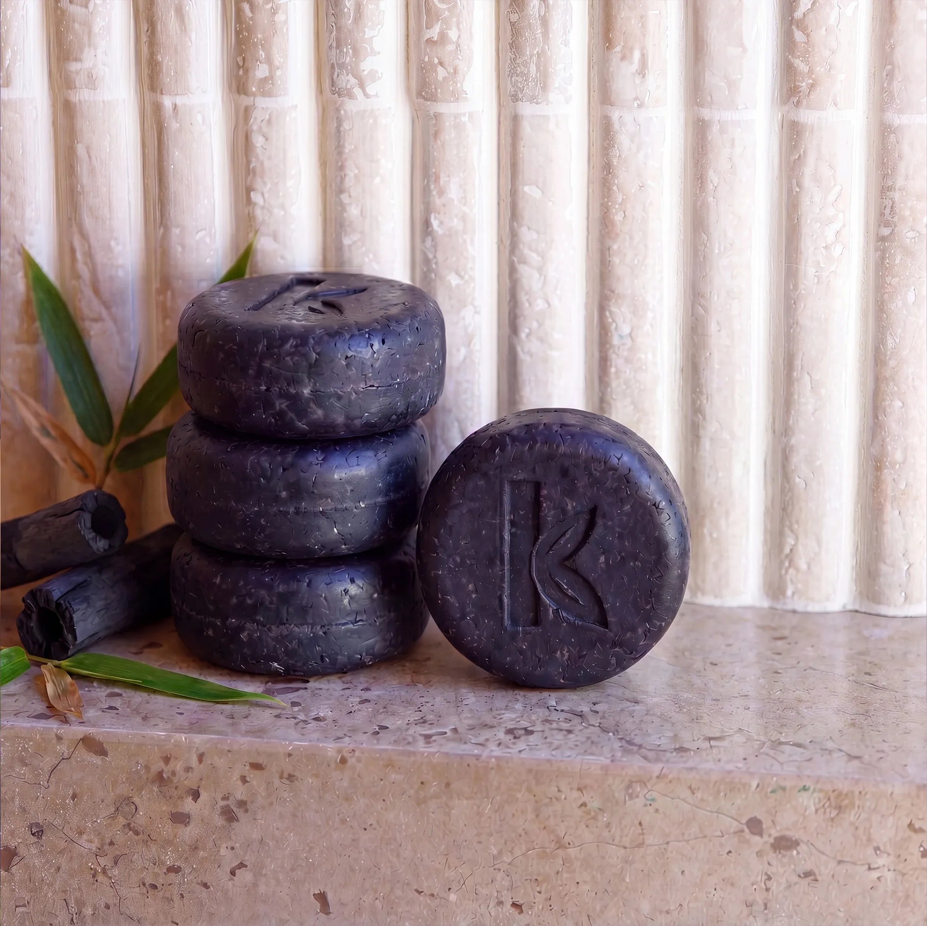Stack of charcoal shampoo bars with a logo on a stone surface