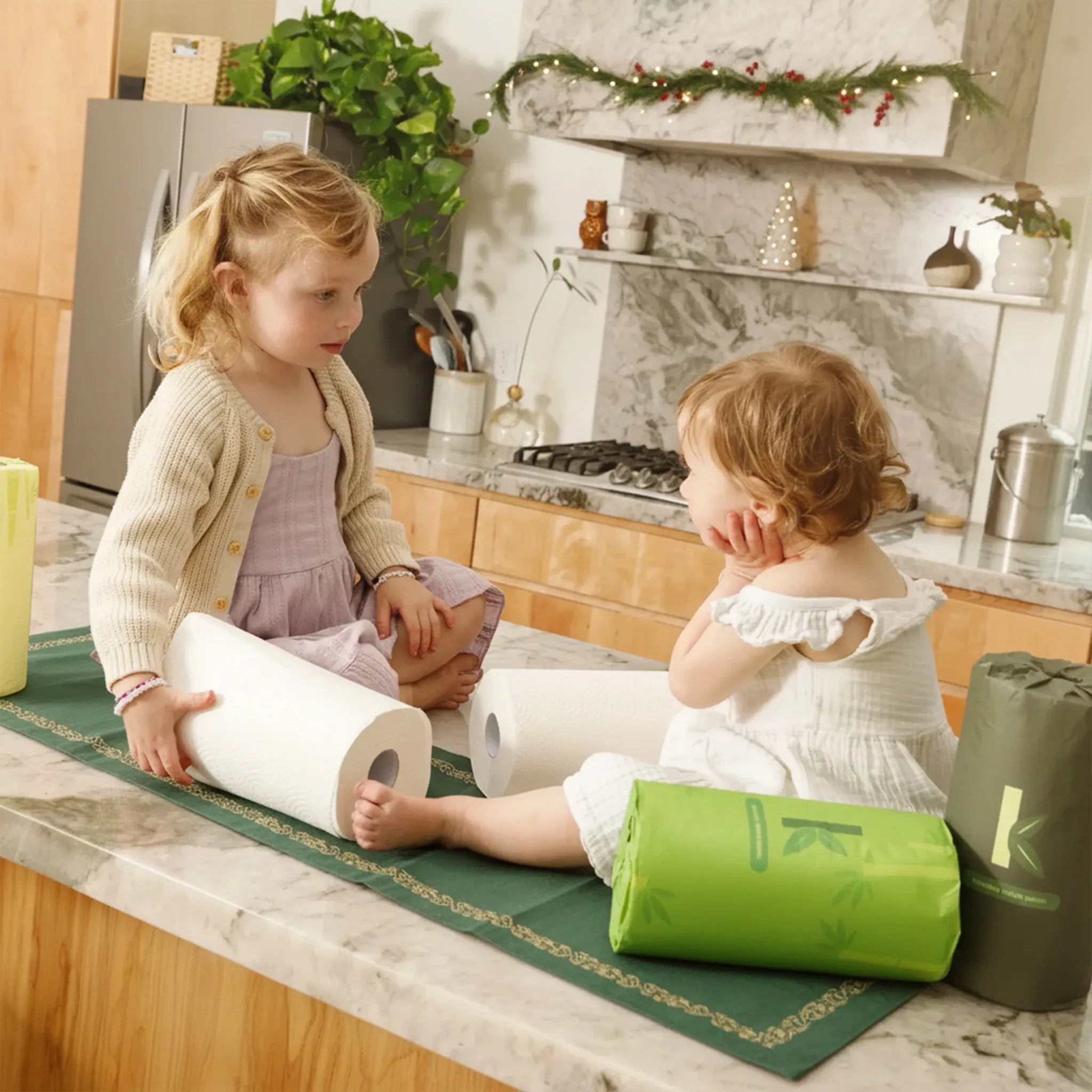 Two young children playing with bamboo paper towels on a kitchen counter.