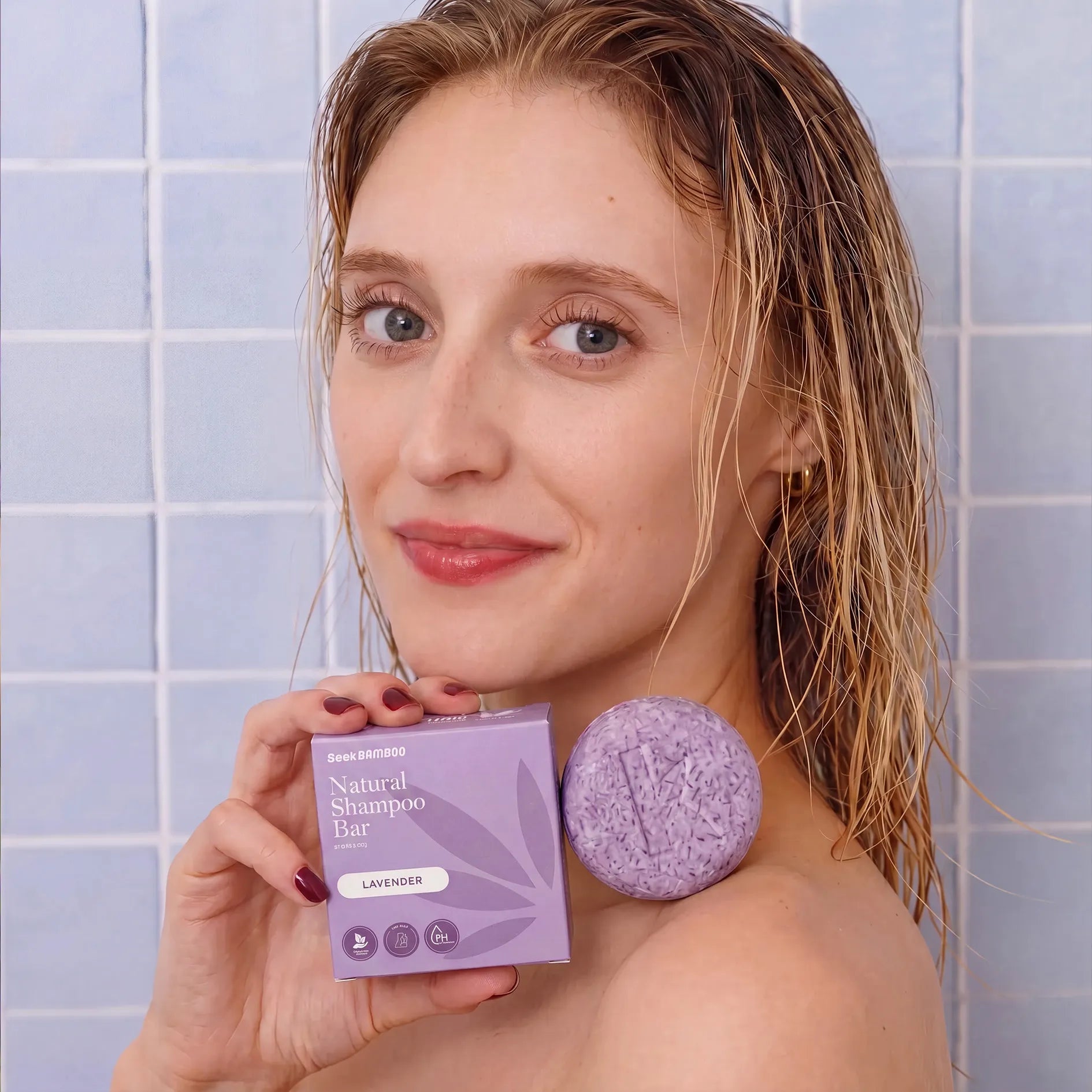Woman holding a natural lavender shampoo bar and packaging in a bathroom setting