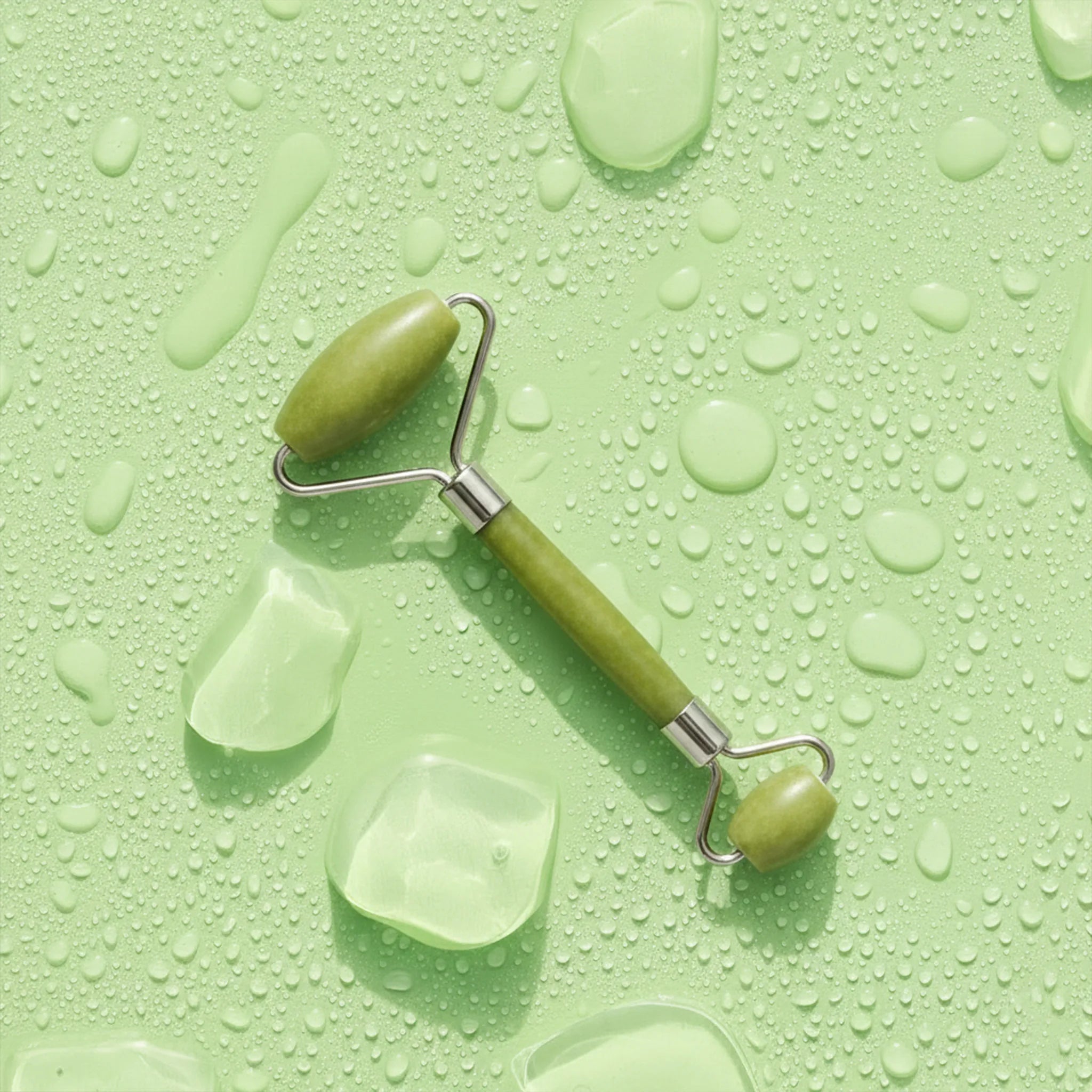 Green facial roller on a green background with water droplets