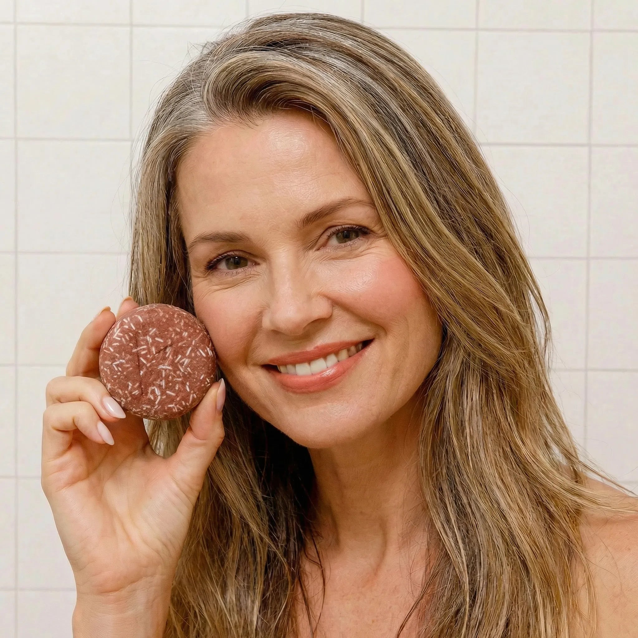 Woman holding a polygonum shampoo bar in front of a tiled wall