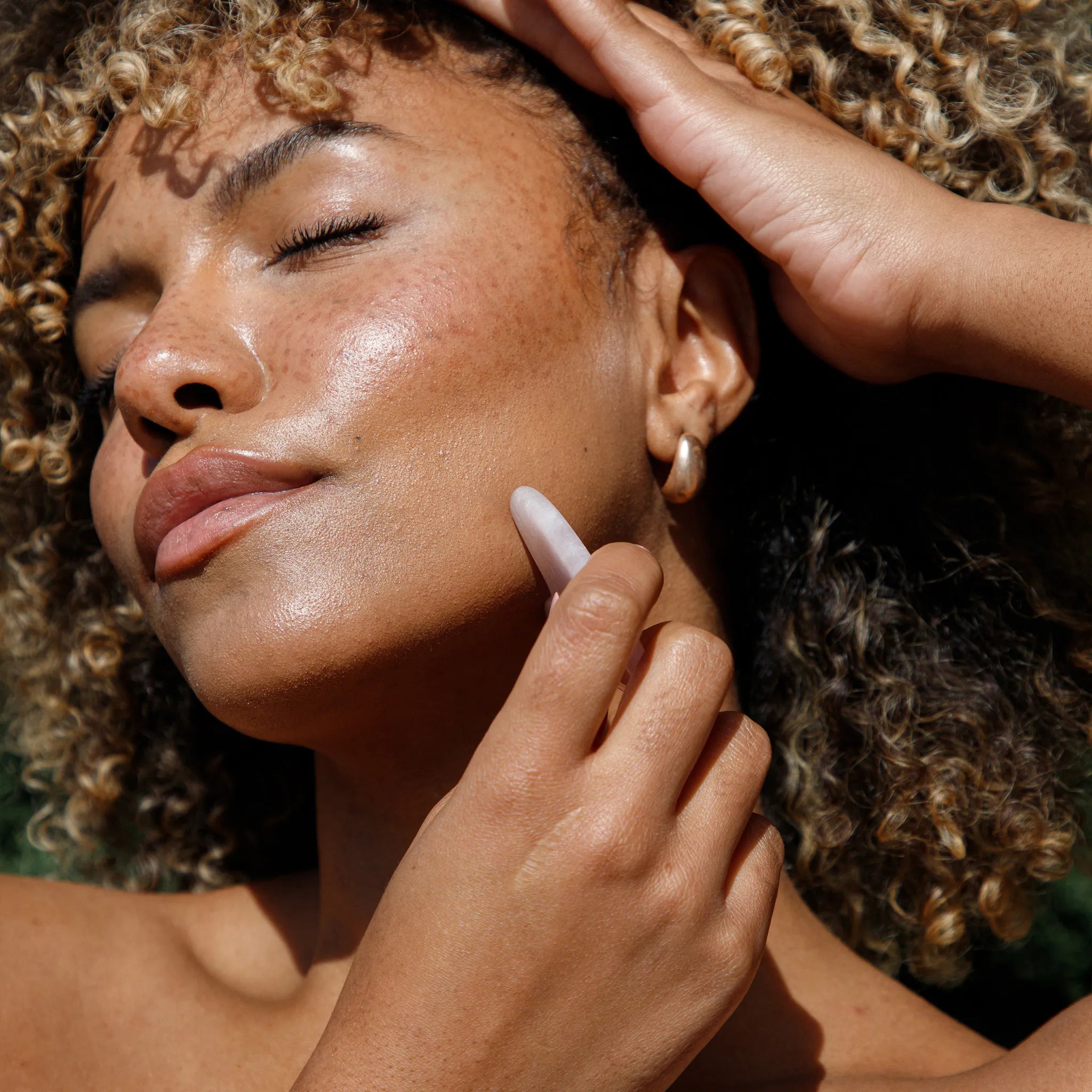 Close-up of a person applying rose quartz gua sha to face.