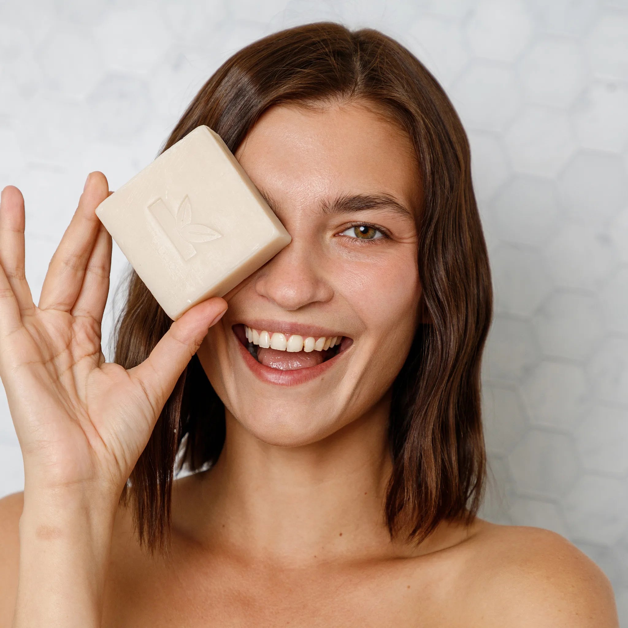 a woman holding a rosemary soap from seek bamboo up to her face