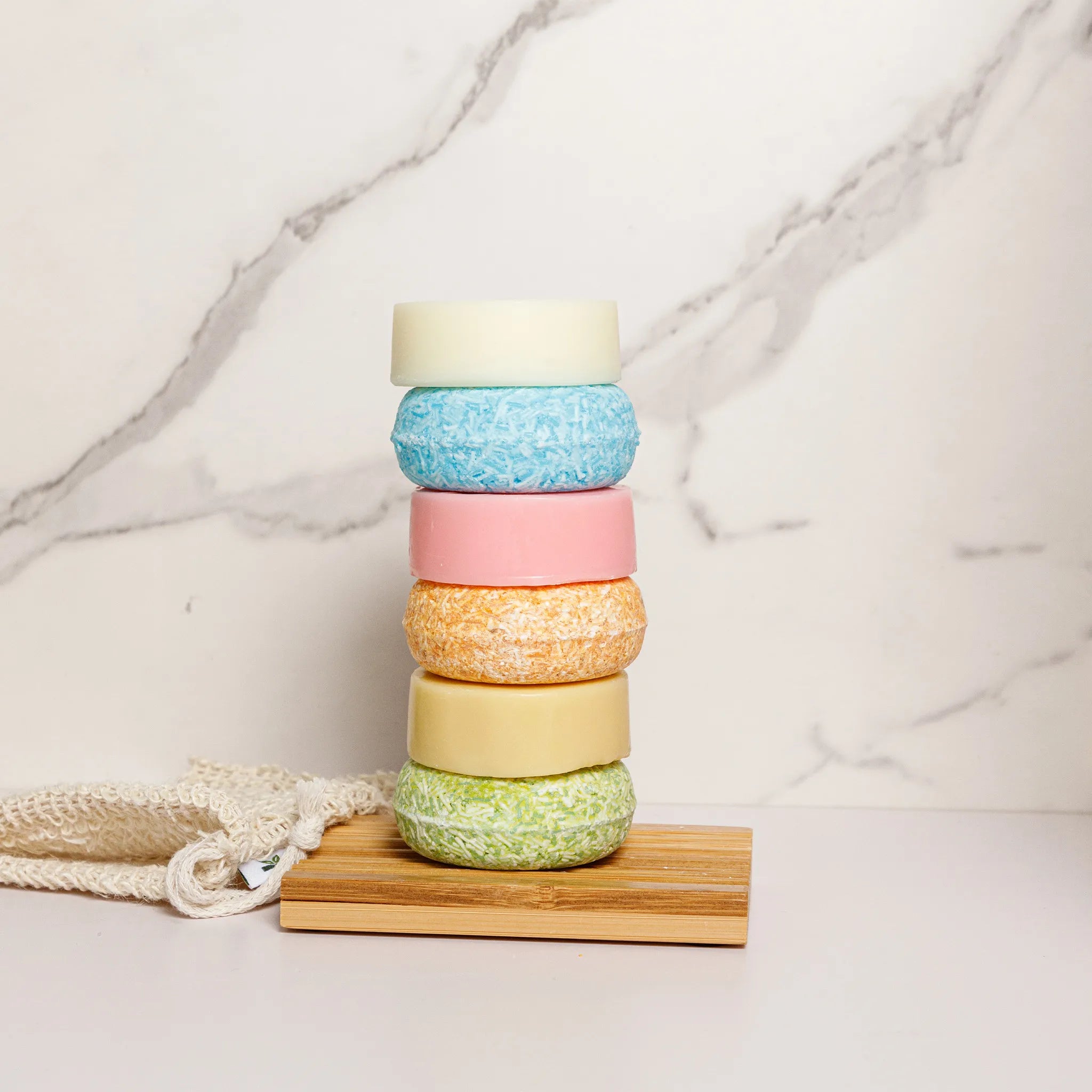Stack of colorful shampoo bars and conditioner on a wooden block with a marble background.